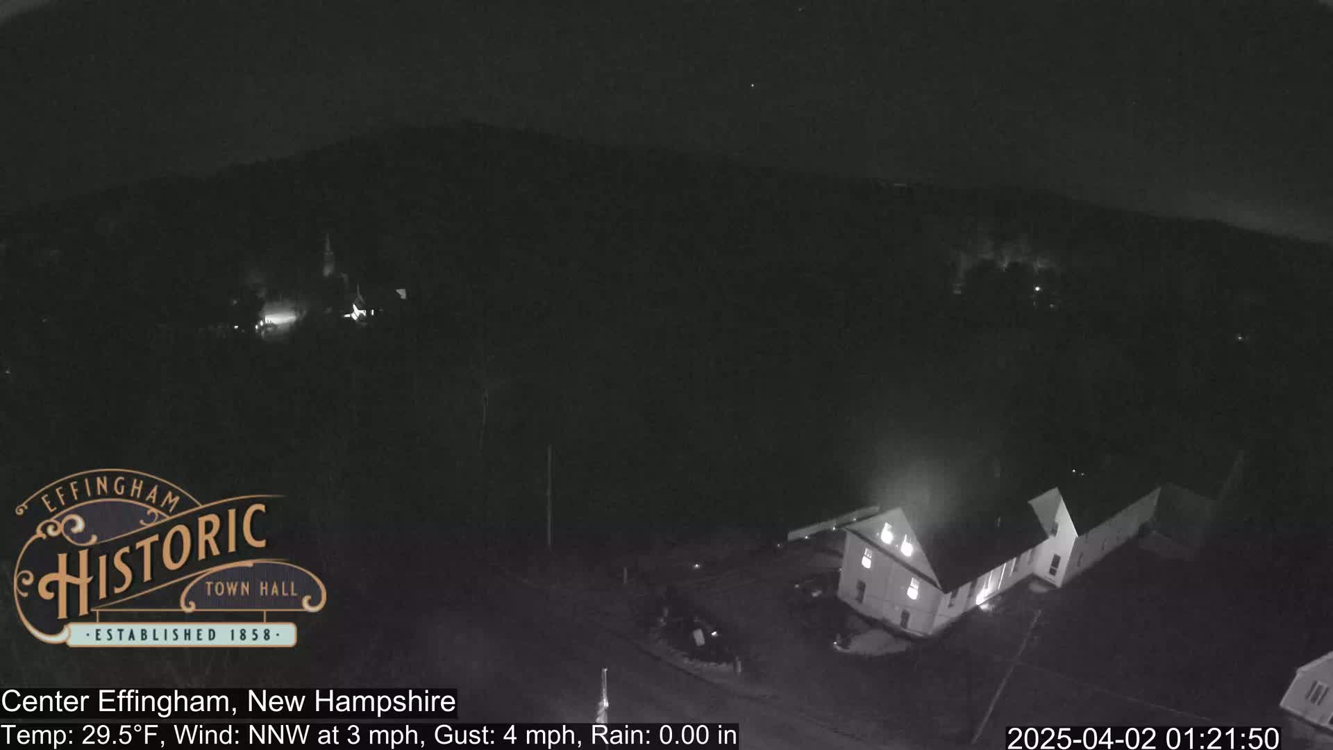 A nighttime, low-light aerial view shows a building and surrounding area under a dark sky with a temperature of 29.5°F, a northwest wind at 3 mph, and gusts up to 4 mph.