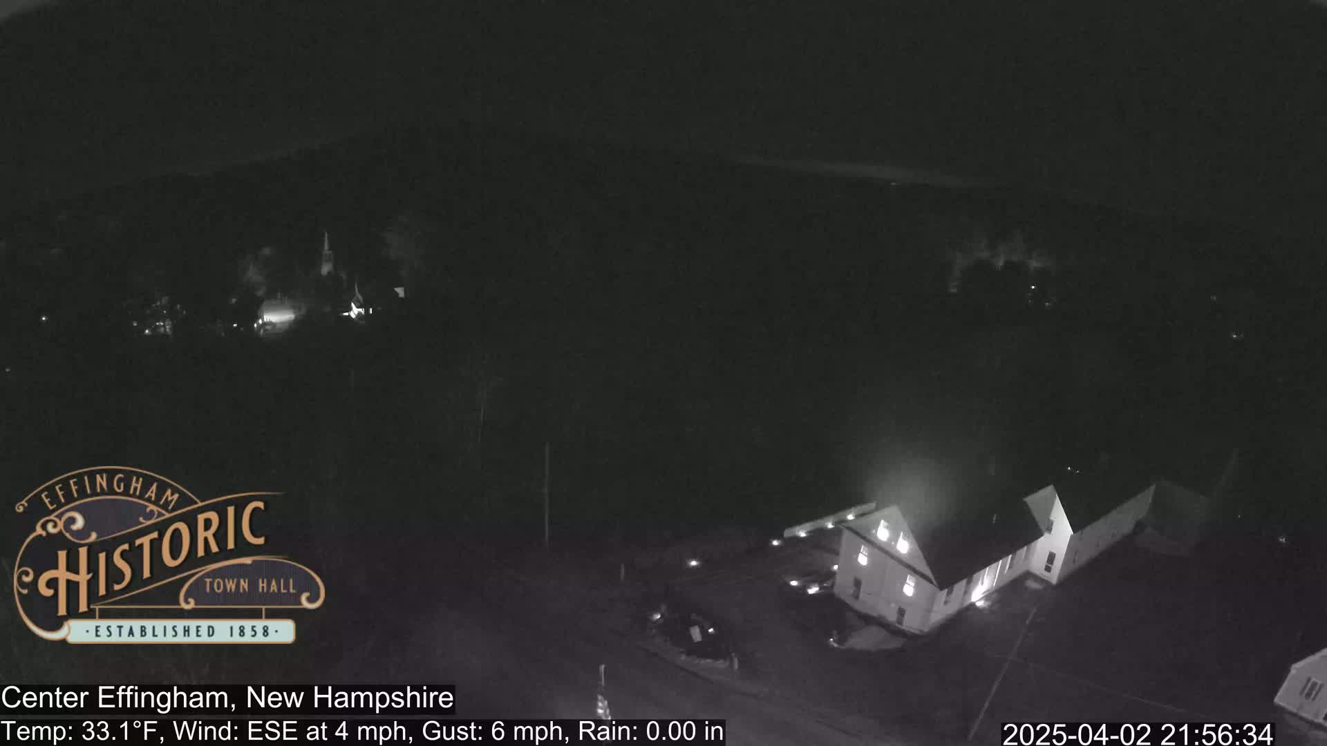 A nighttime, low-light aerial view of a building complex and surrounding area with a light wind.