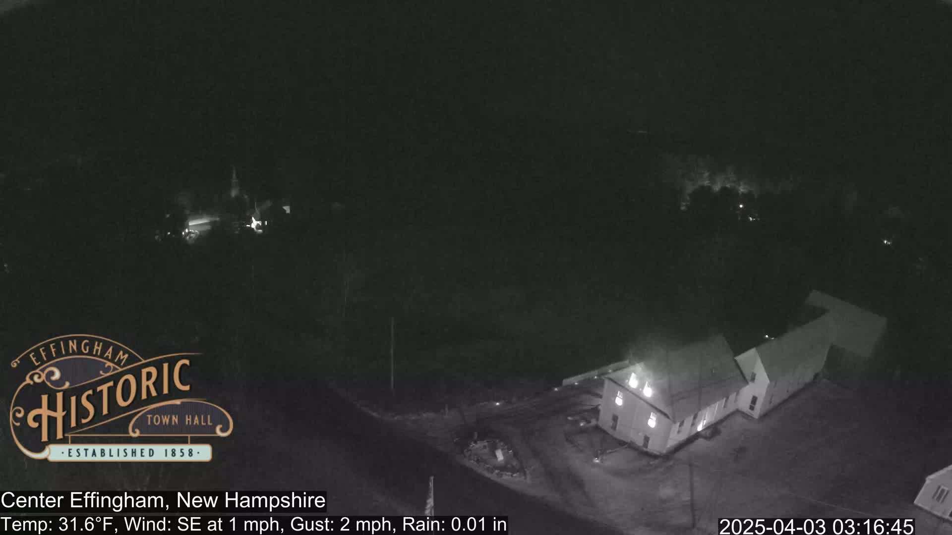 A nighttime, aerial view of a building complex under light rain with a southeast wind.