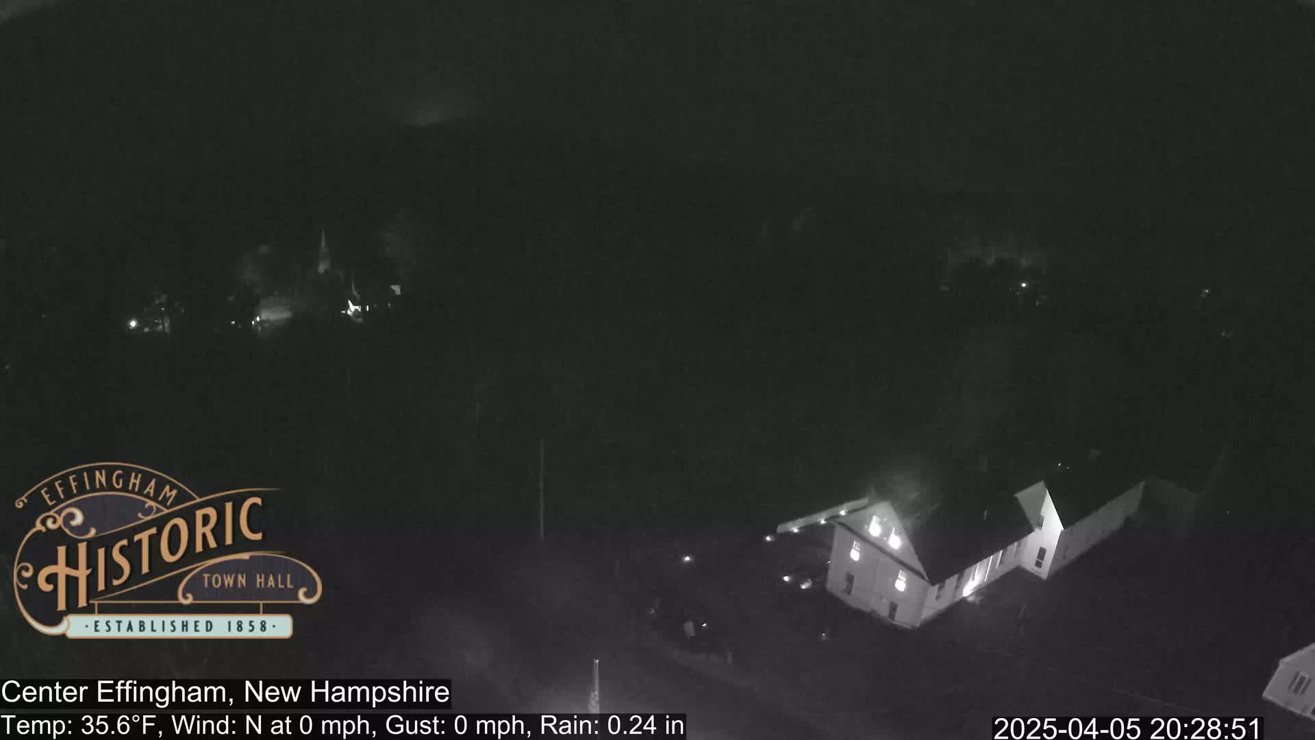 A nighttime, low-light view of a building complex under rainy conditions.
