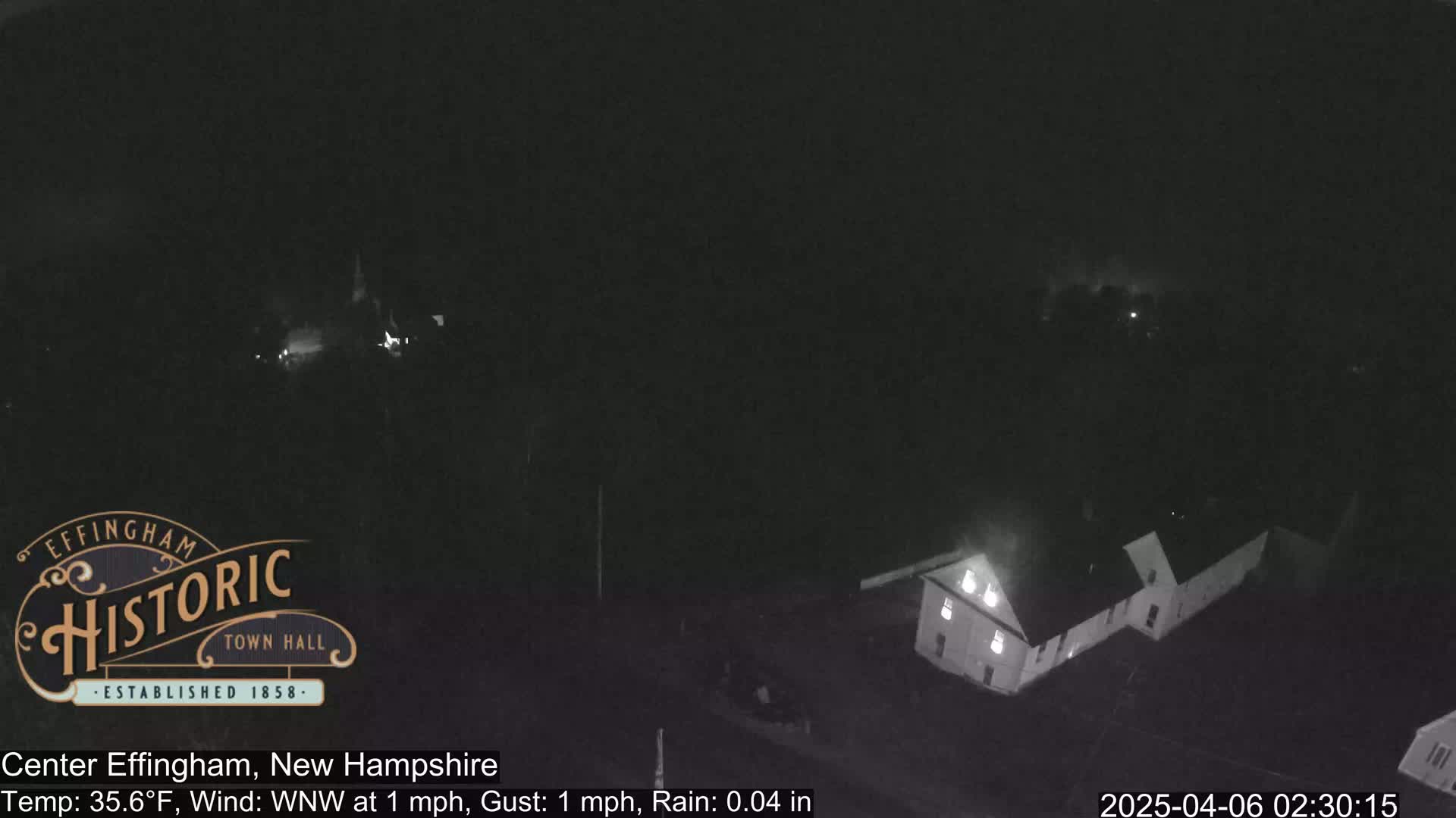 A nighttime, low-light view of a building complex under rainy conditions with a temperature of 35.6°F and a light wind.