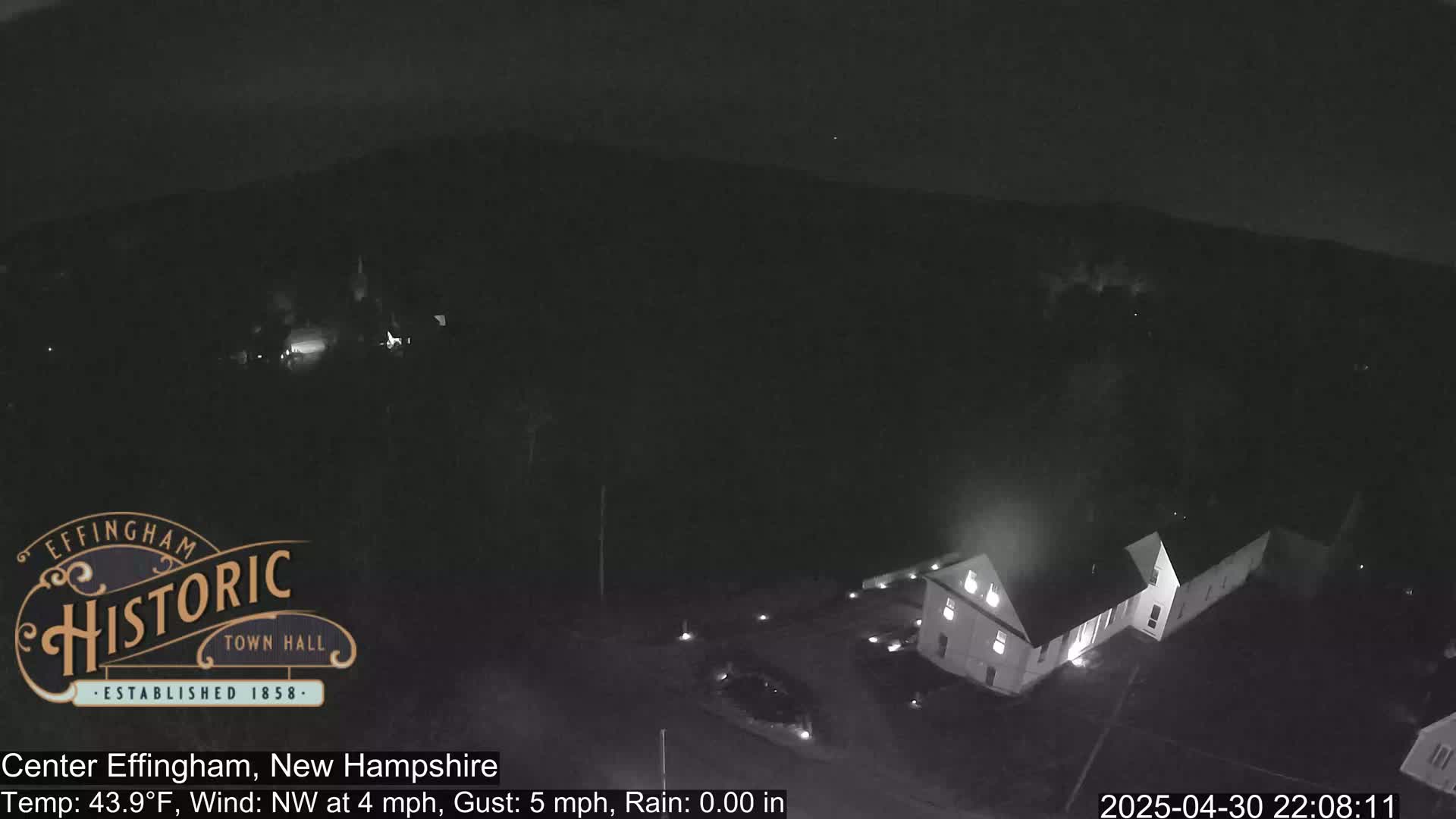 A nighttime aerial view shows a building complex in a dimly lit area with a northwest wind at 4 mph and a 5 mph gust.