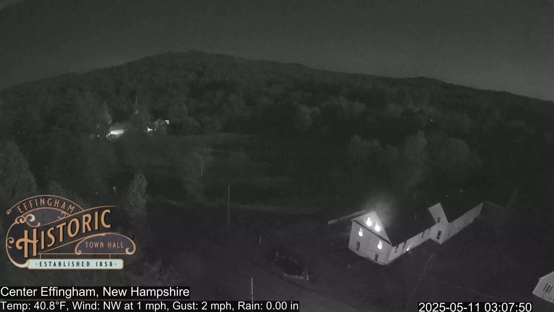 A nighttime, low-light view of a building and surrounding wooded area, with a calm northwest wind and no rain.