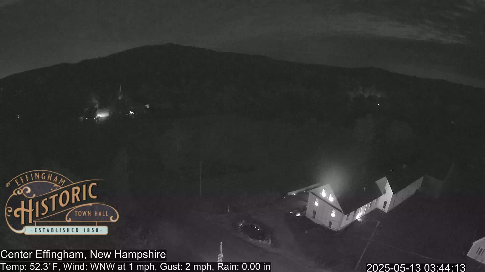 A nighttime, low-light view of a building and a hill under a clear, dark sky with a slight wind.