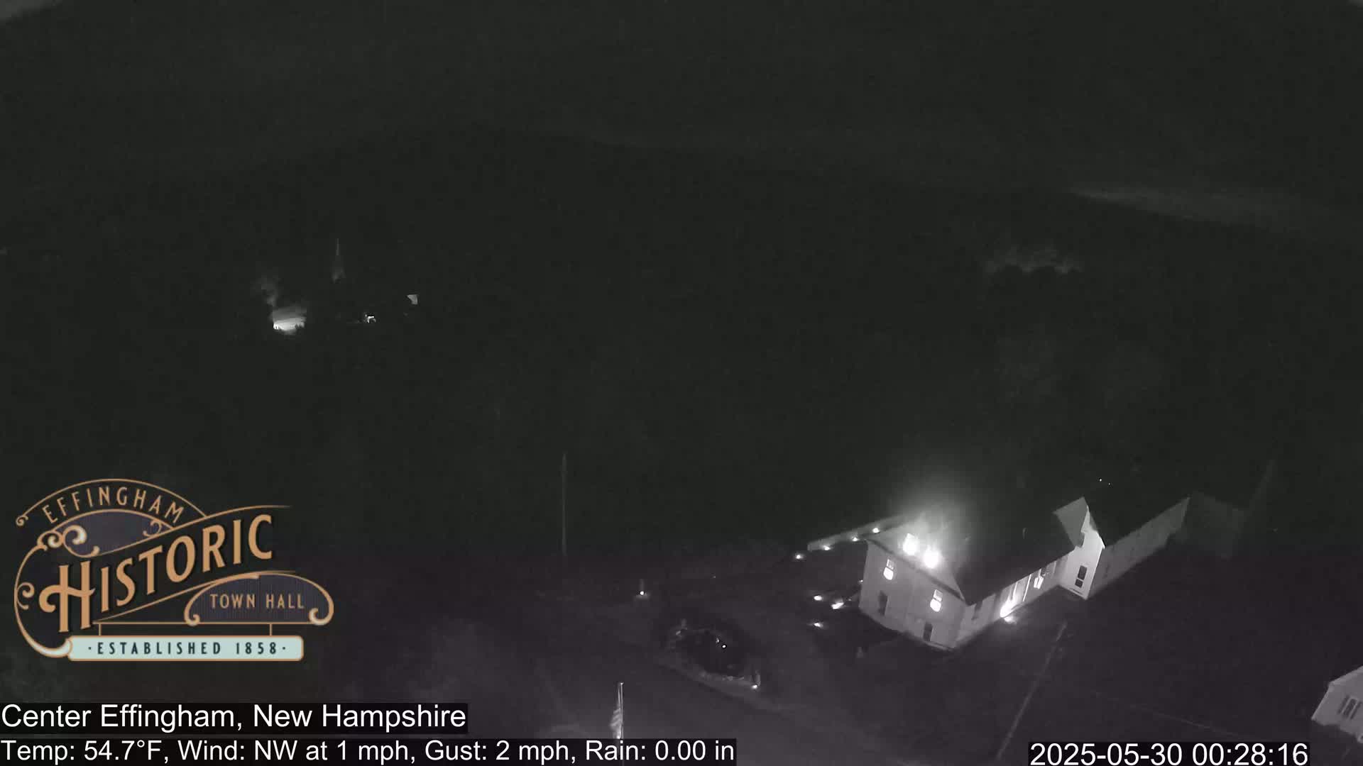 A nighttime, aerial view shows a building with lights on, under a dark, rainless sky with a slight northwest wind.