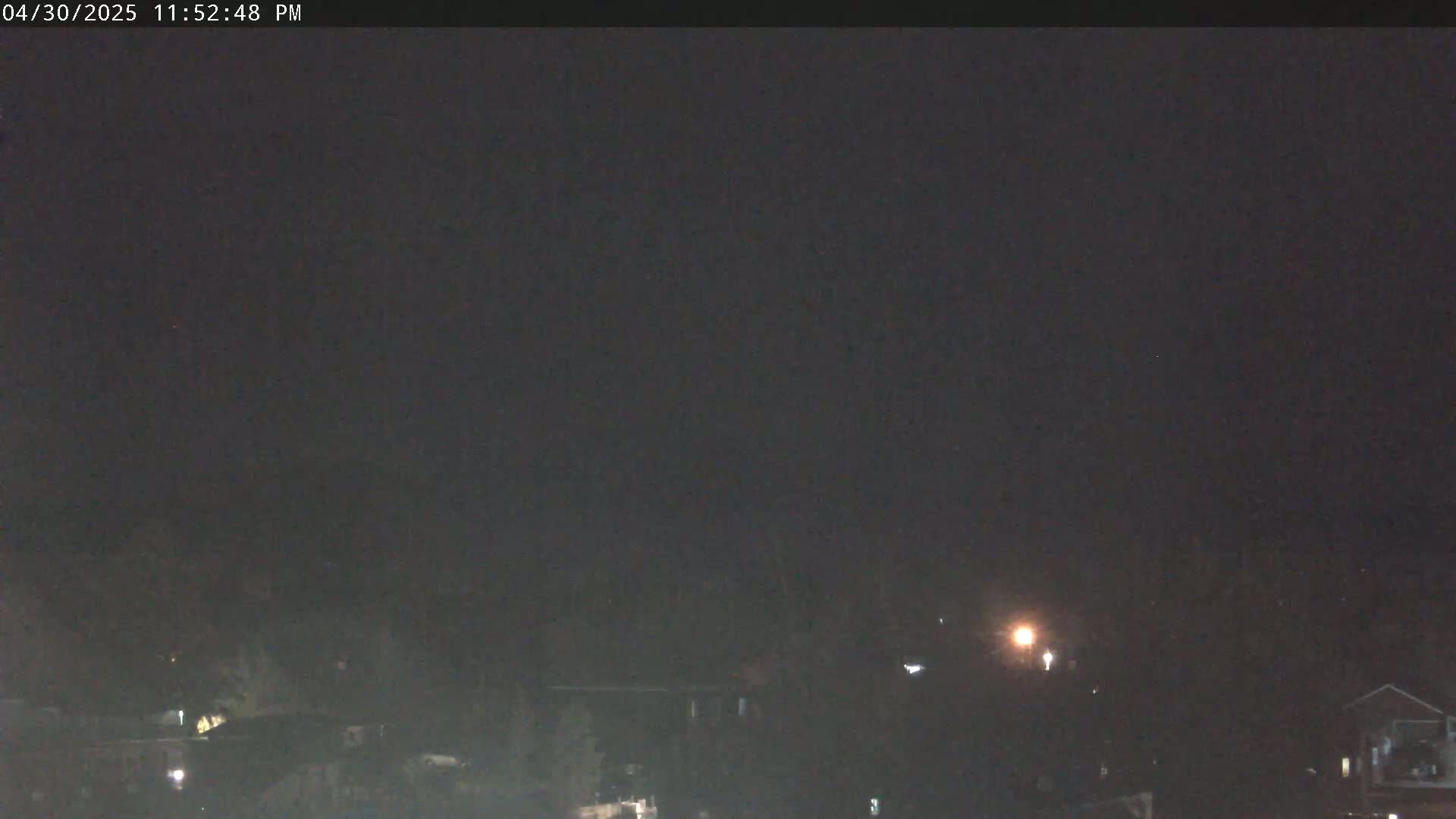 A nighttime, dark view of a residential area with dimly lit houses under a mostly clear sky.