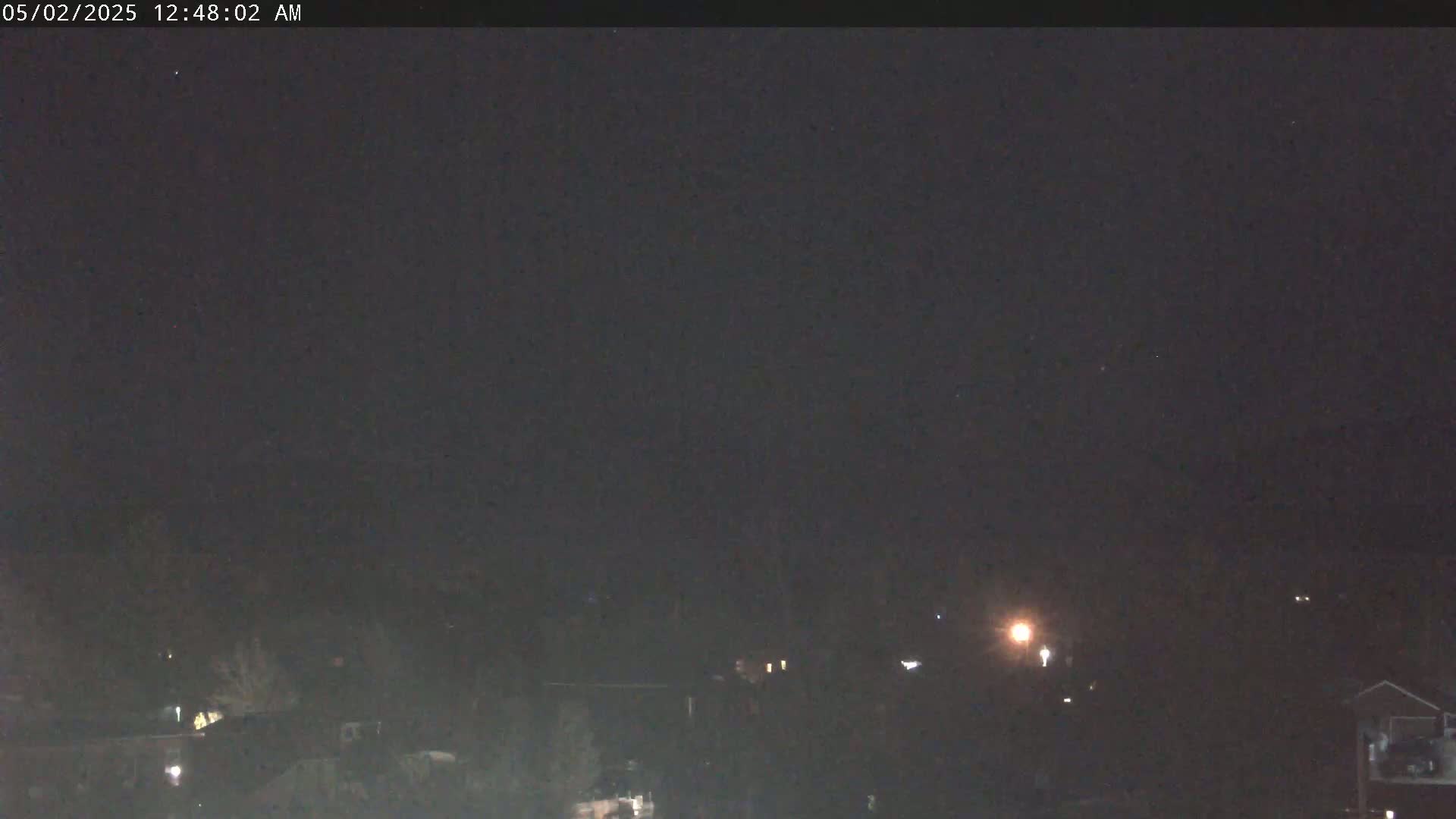 A dark, nighttime view shows dimly lit houses and trees under a clear, black sky.