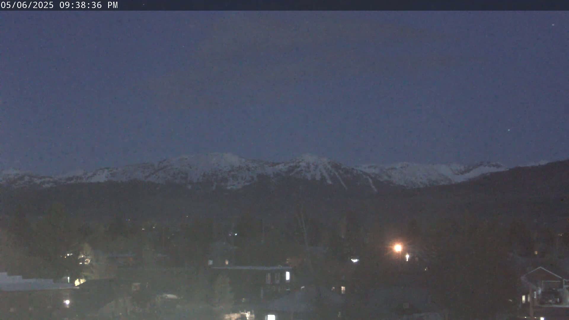 Snow-capped mountains are visible in the distance under a twilight sky over a dark town at night.