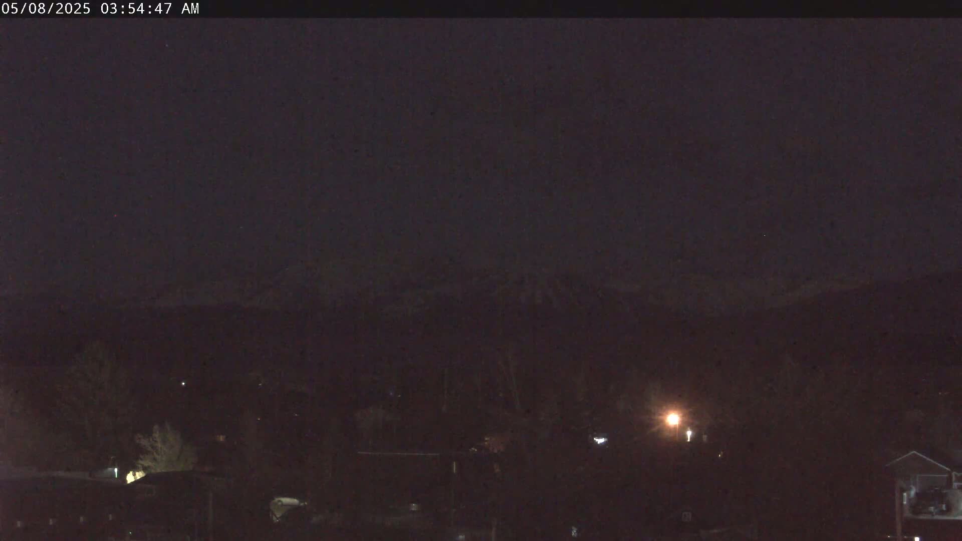 A dark, nighttime scene shows a snow-capped mountain range in the distance, above a dimly lit town.