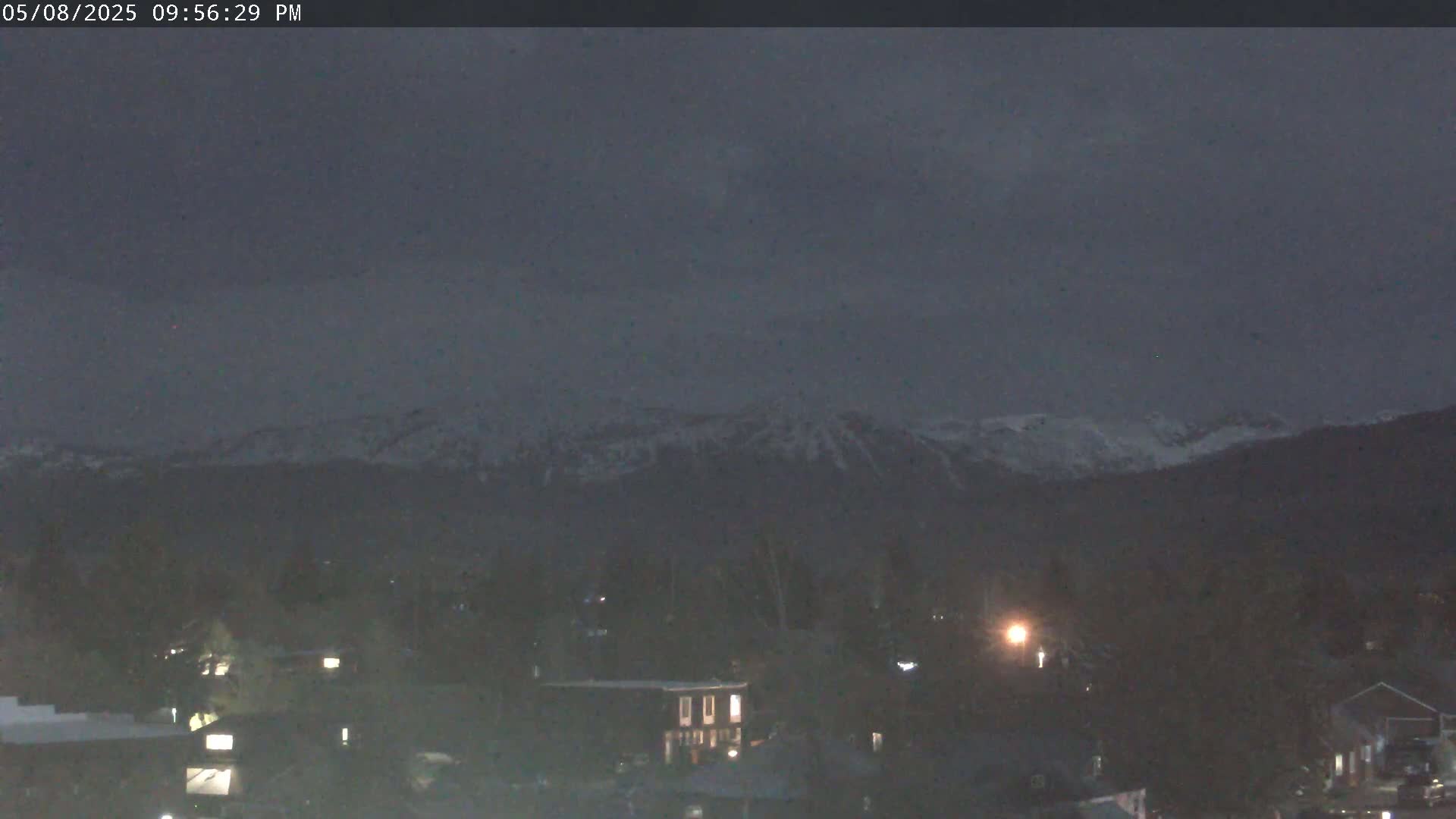 Snow-capped mountains are visible in the distance under a dark, overcast sky above a town at night.