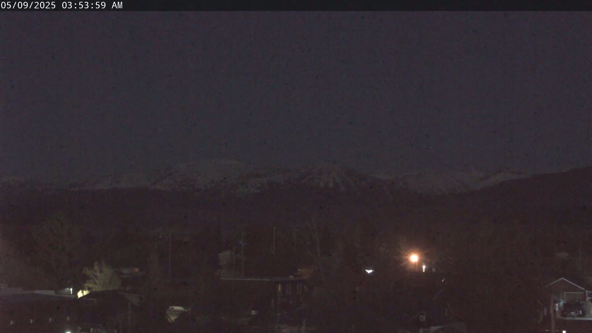 A snow-capped mountain range is visible in the distance under a dark, nighttime sky over a dimly lit town.