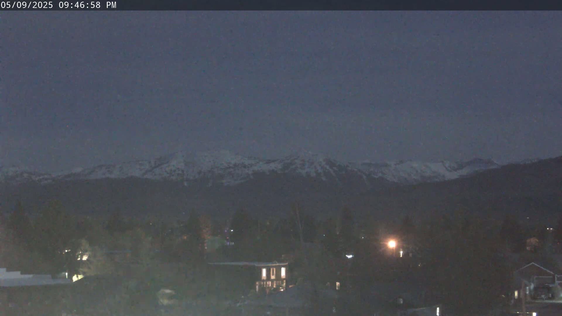 Snow-capped mountains are visible in the distance above a dark, nighttime town.