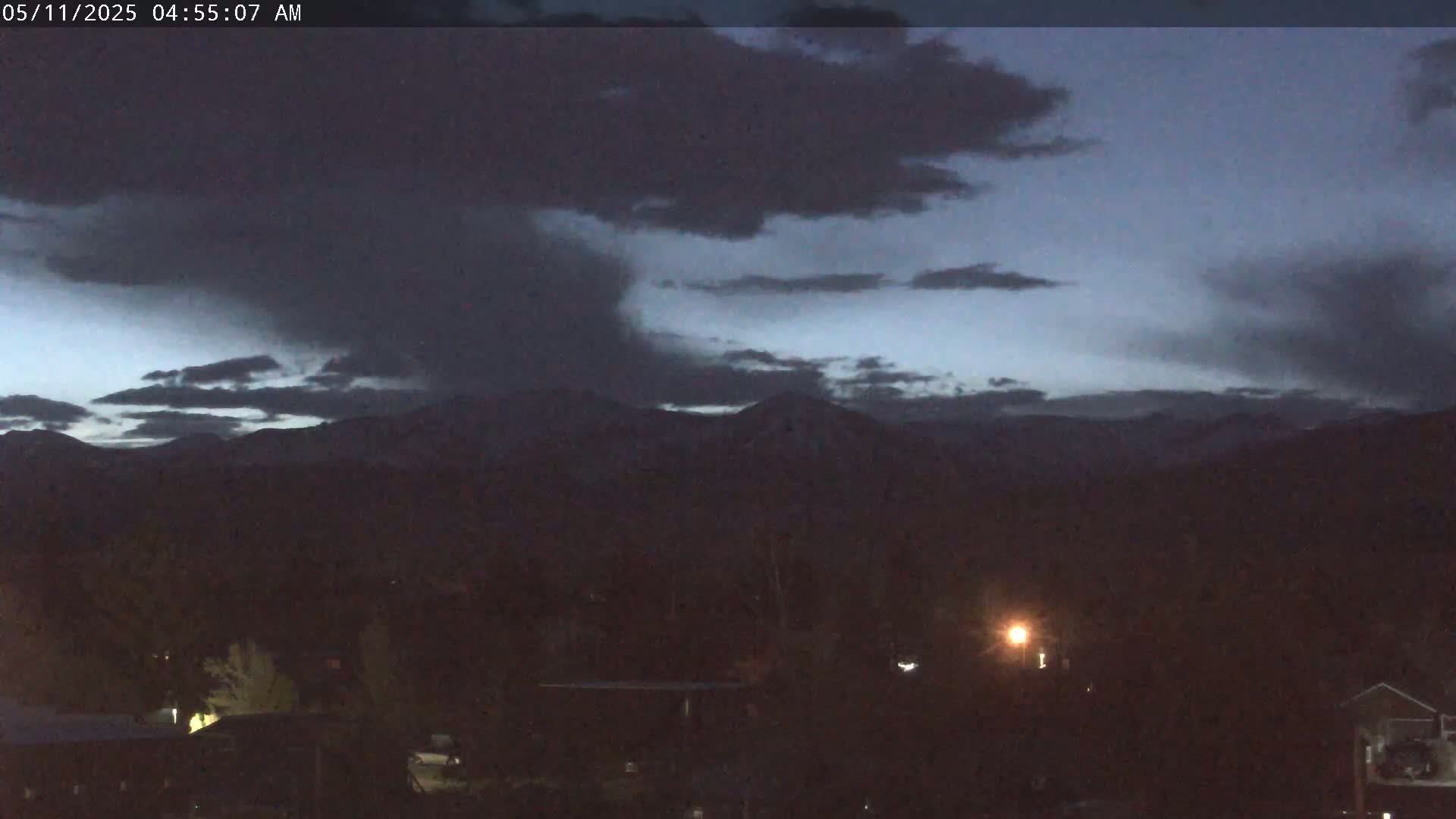 Snow-capped mountains are visible in the pre-dawn darkness under a mostly cloudy sky.
