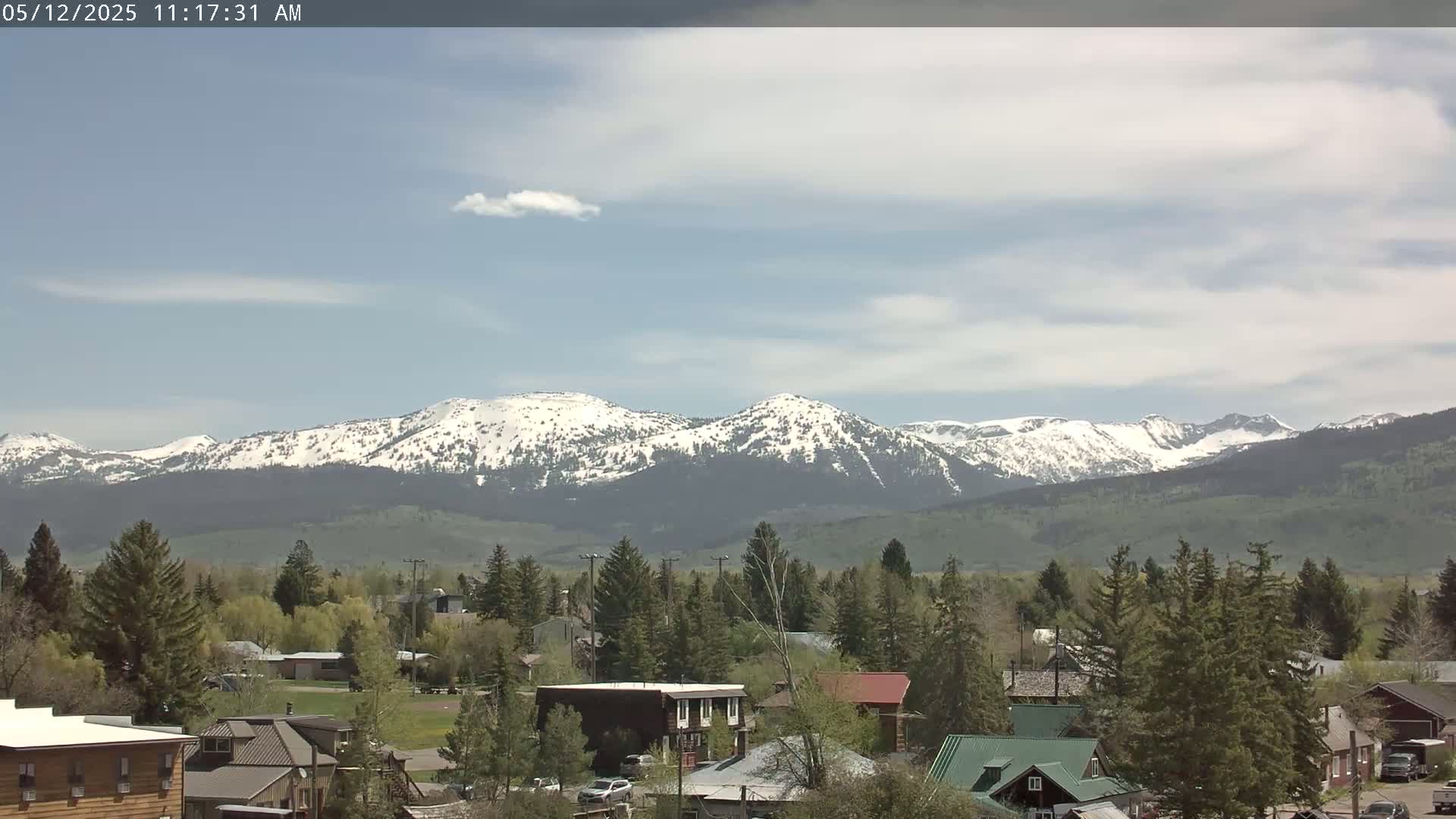 A partly cloudy day reveals a small town nestled in a valley, with snow-capped mountains in the background.