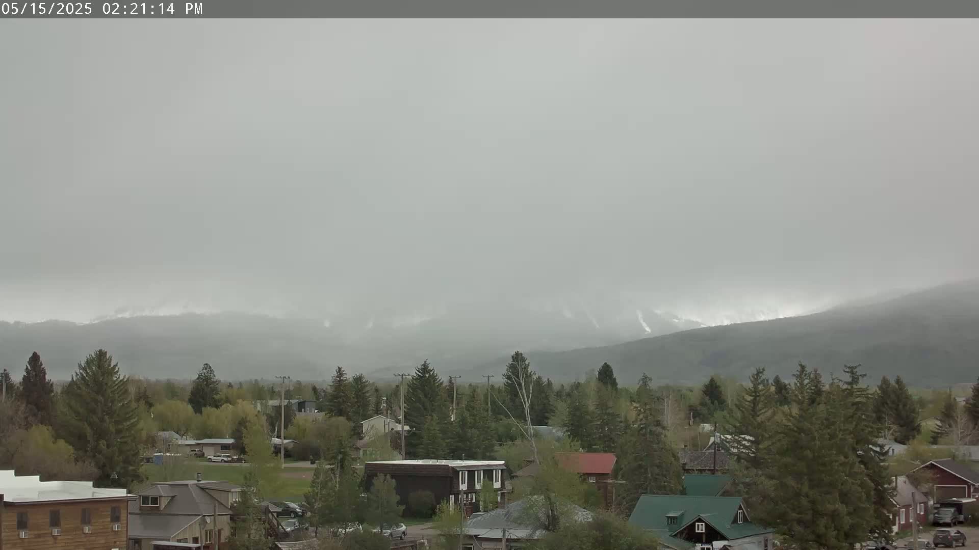 A small town nestled among green trees and hills, with a hazy, overcast sky.
