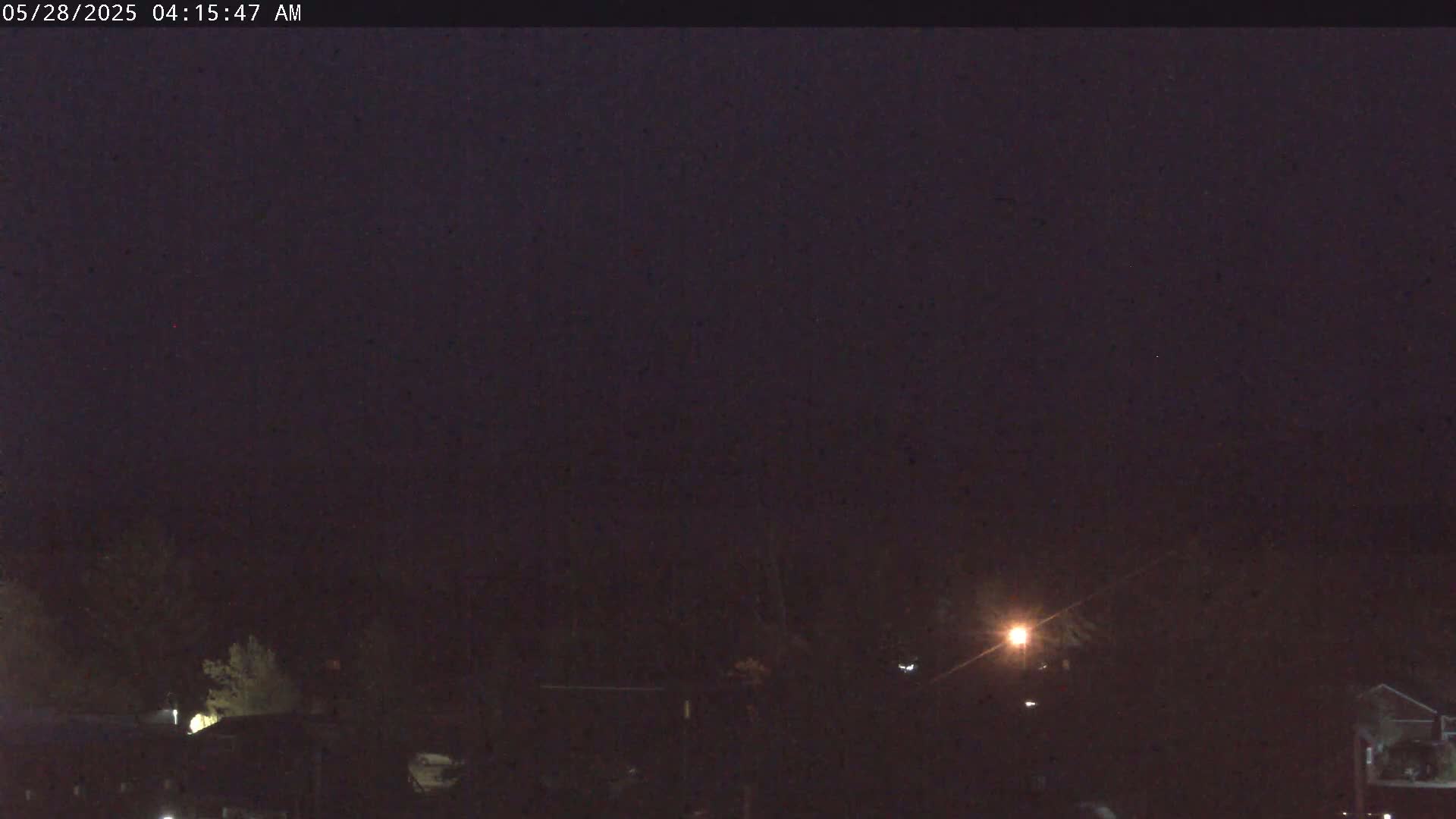 A dark, nighttime scene shows a few dimly lit buildings and trees under a mostly clear, dark purple sky.