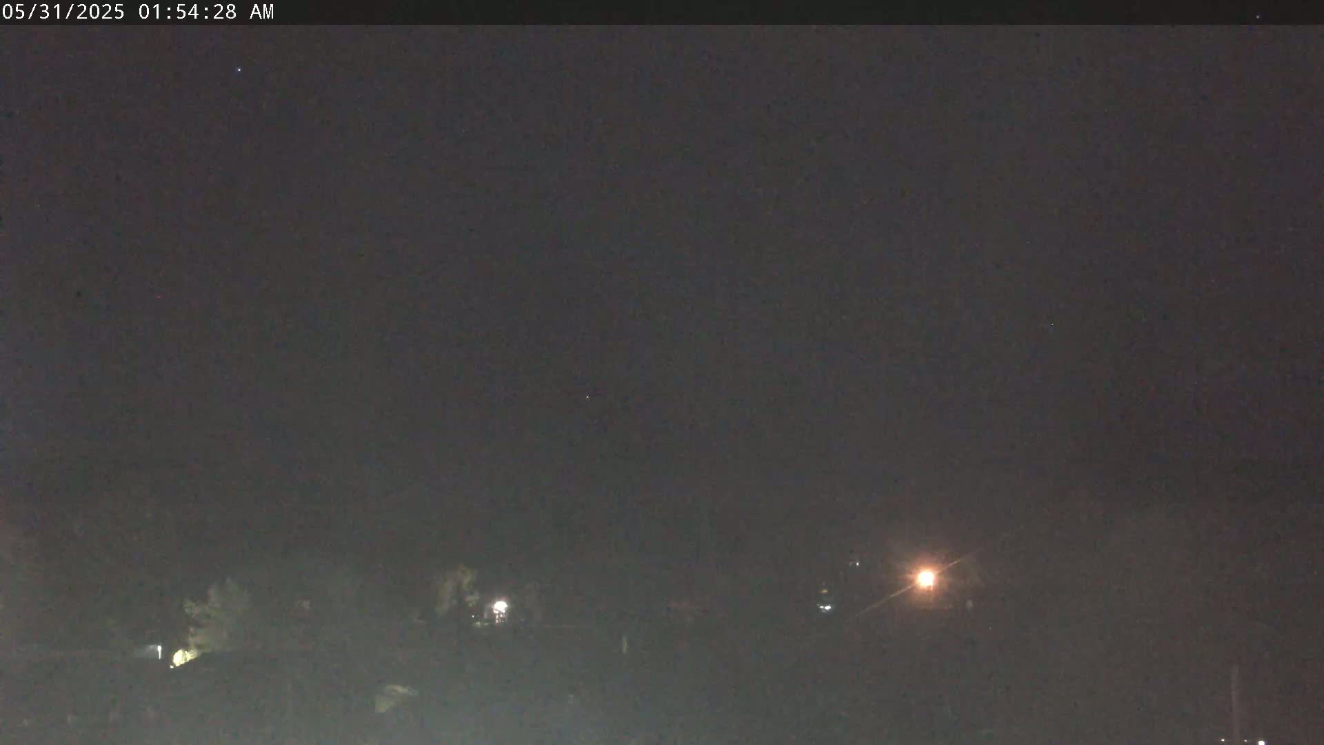A nighttime, low-light view of a dark landscape with a few distant lights visible.