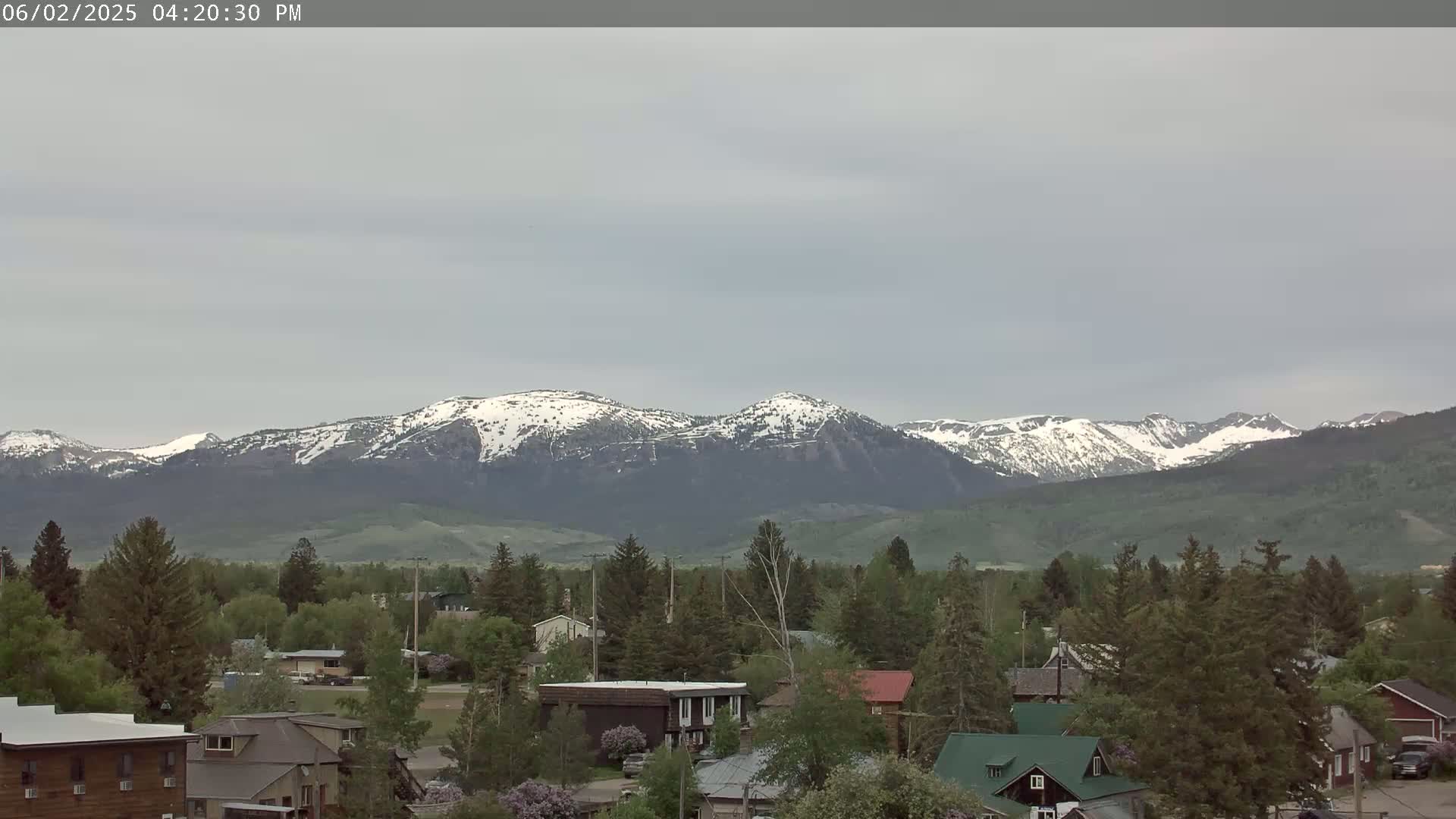 Snow-capped mountains are visible in the distance behind a small town under an overcast sky.