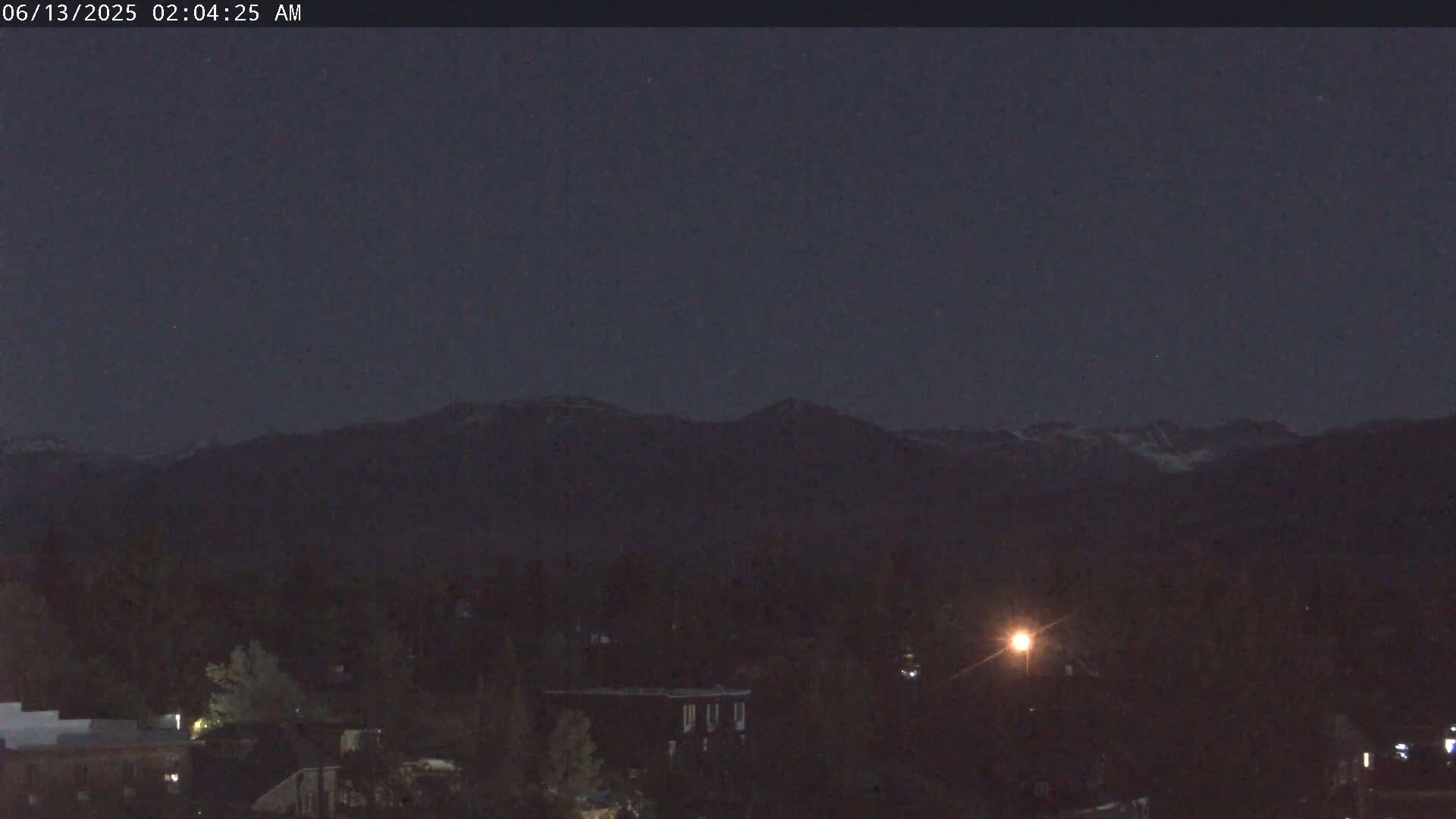 A nighttime view of a town nestled beneath a dark mountain range under a clear, dark sky.