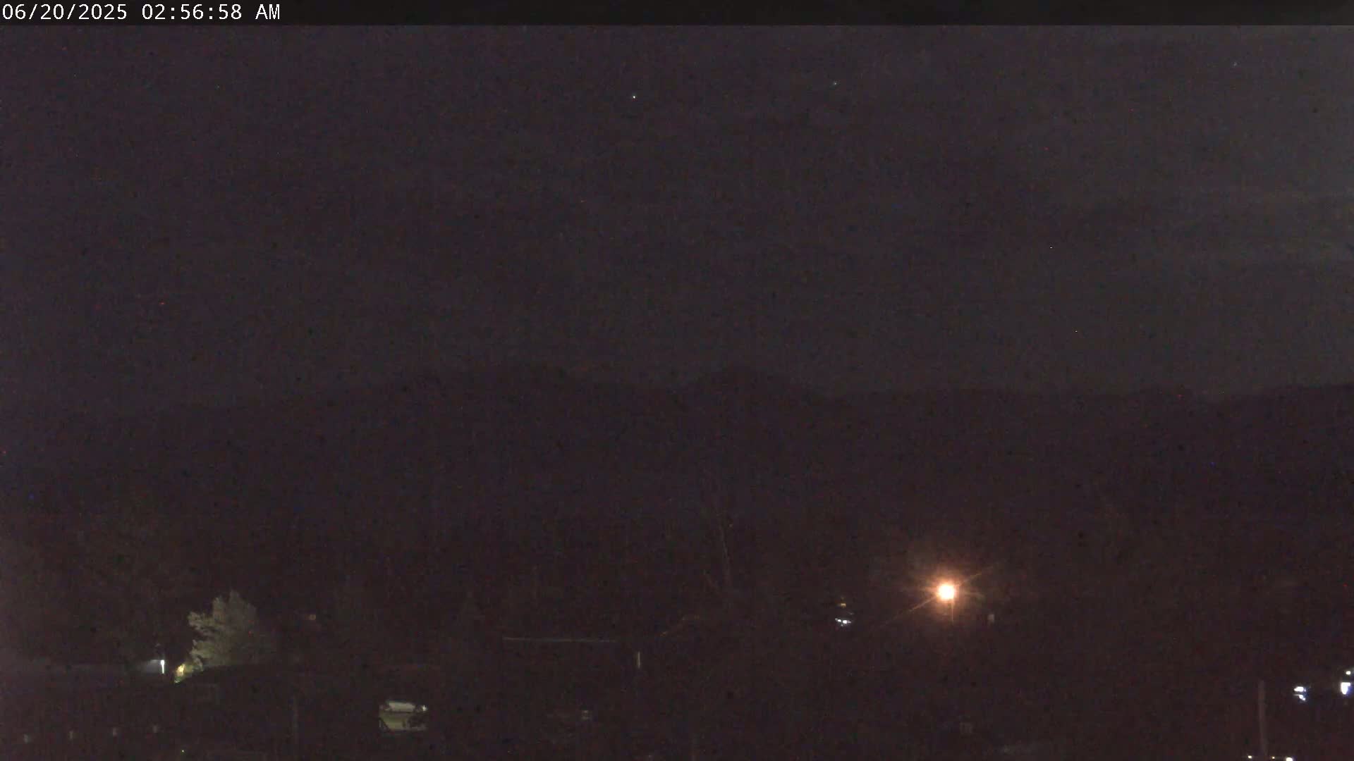 A nighttime view of dark, silhouetted trees and hills under a clear, dark sky.
