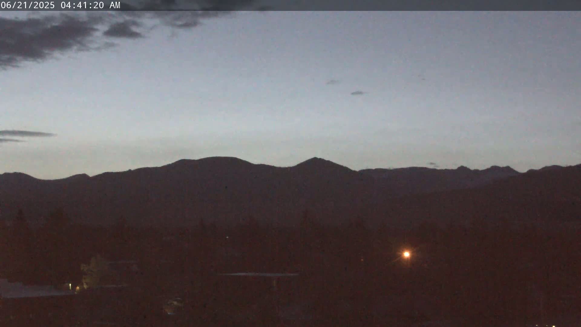 A dark, mountainous landscape is visible under a dusky, cloudy sky before dawn.