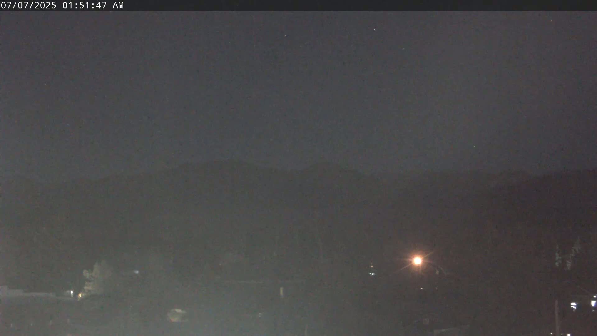 A nighttime, dark view of a dimly lit landscape with a distant mountain range under a clear sky.