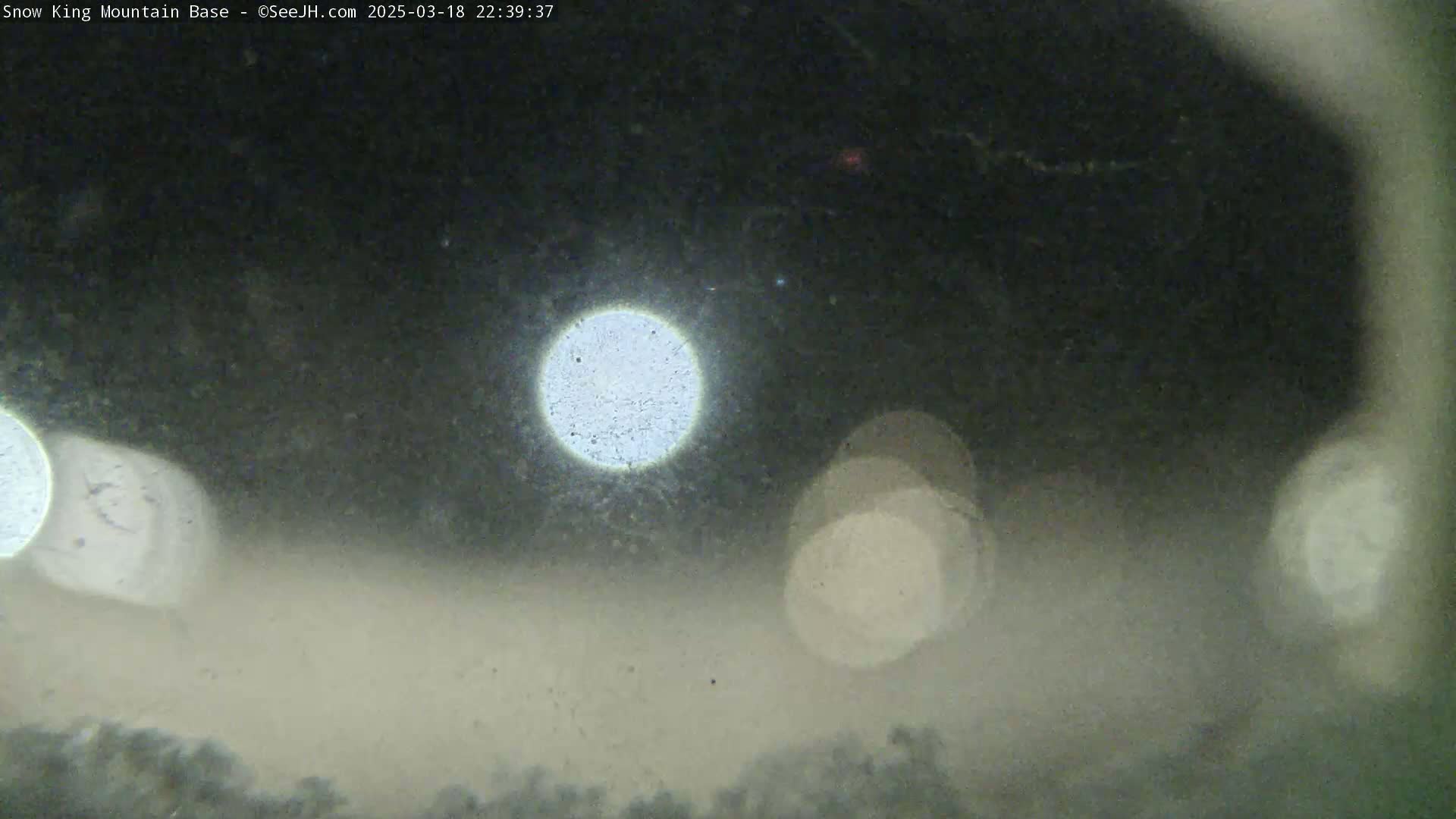 A blurry, nighttime image shows out-of-focus lights and a hazy, possibly snowy, landscape.