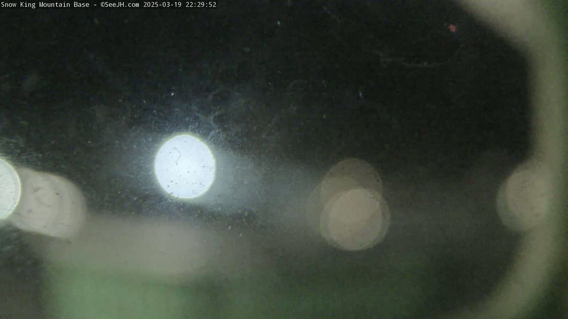 Blurred nighttime view showing out-of-focus lights through a dirty or fogged surface.