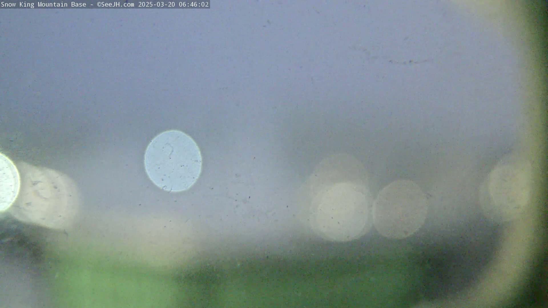 A blurry view of out-of-focus lights and a muted green landscape through a dusty or fogged surface, possibly indicating overcast conditions.