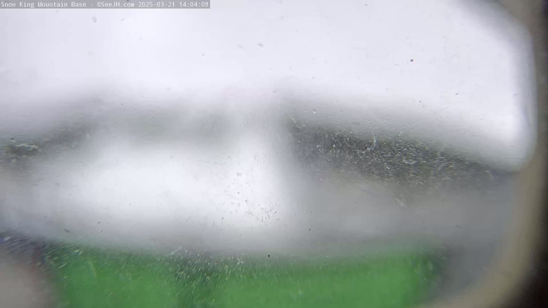 A blurry view of a snowy, overcast scene with a hint of green at the bottom.