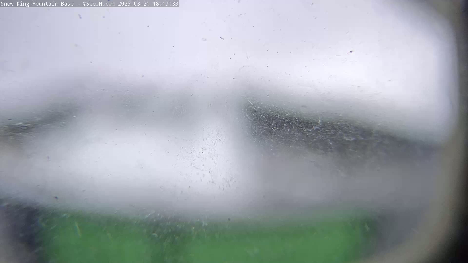 A blurry view of a green object through a snow-covered window in snowy weather.