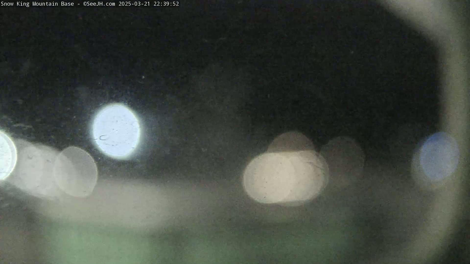 Blurry, out-of-focus nighttime lights are visible through a rain-covered window.