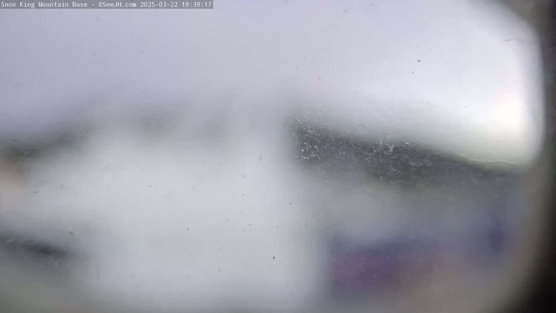 A blurry, snow-filled scene is visible through a snow-covered or fogged-up window.
