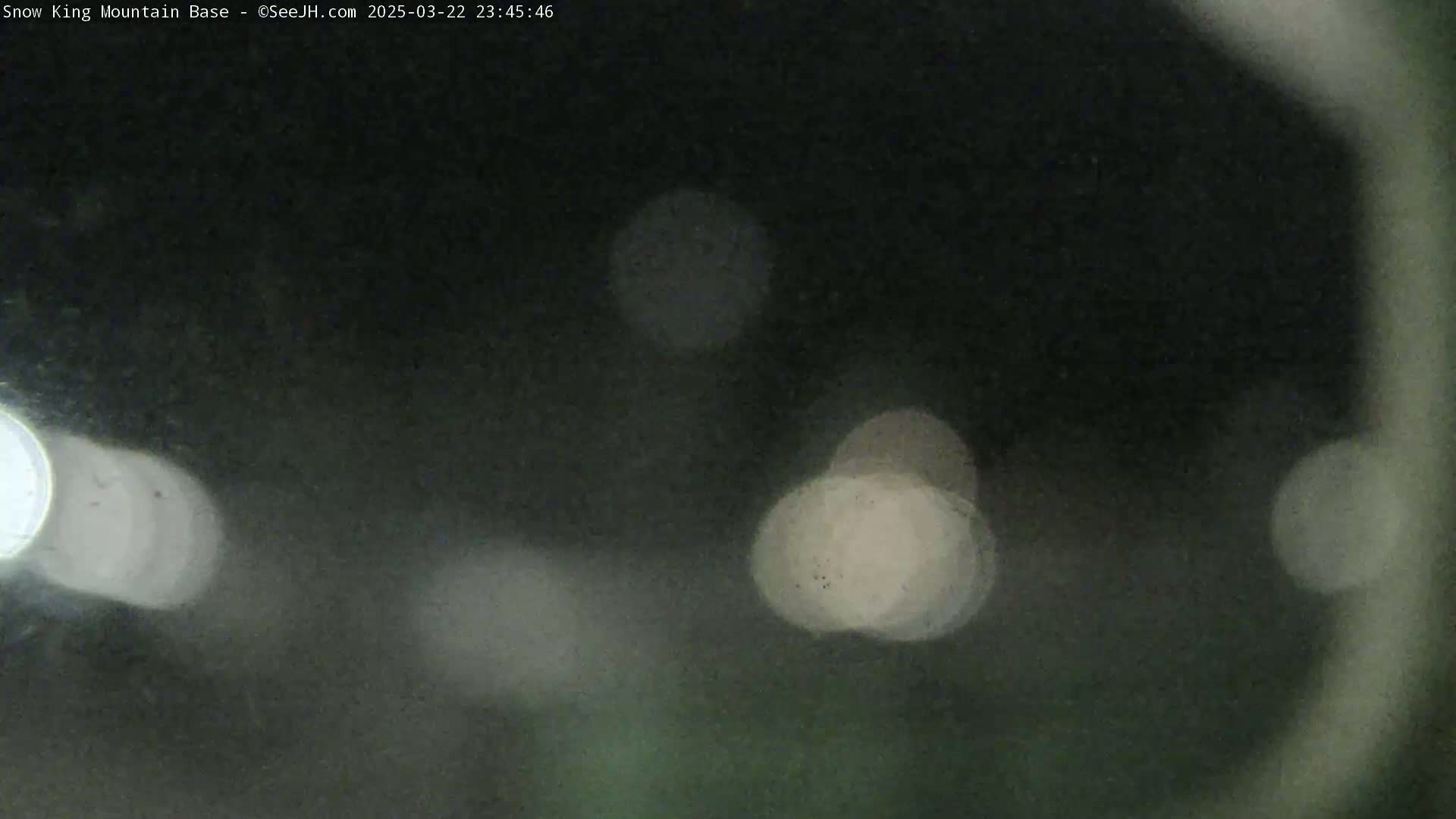 A dark, blurry nighttime image shows out-of-focus lights in the distance through a rain-covered surface.