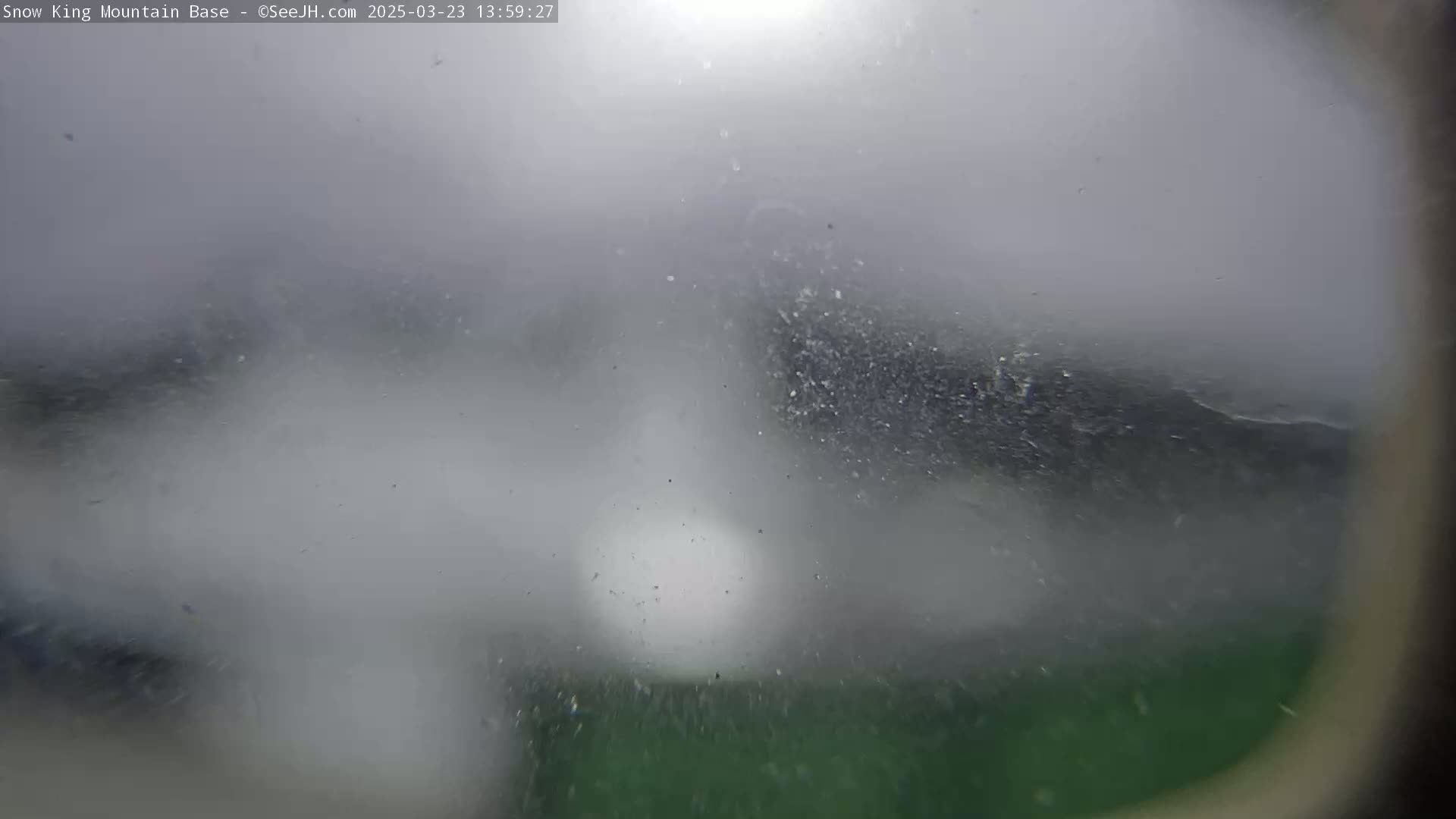 A blurry, hazy view of a dark green landscape is visible through a foggy or snowy, possibly dirty, window or lens.
