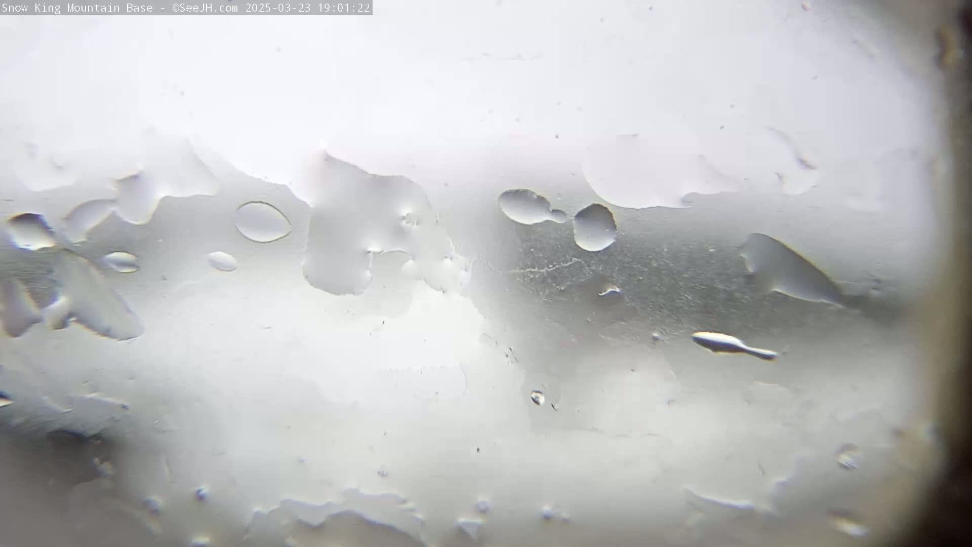 A blurry view through a rain-covered window shows indistinct shapes and water droplets.