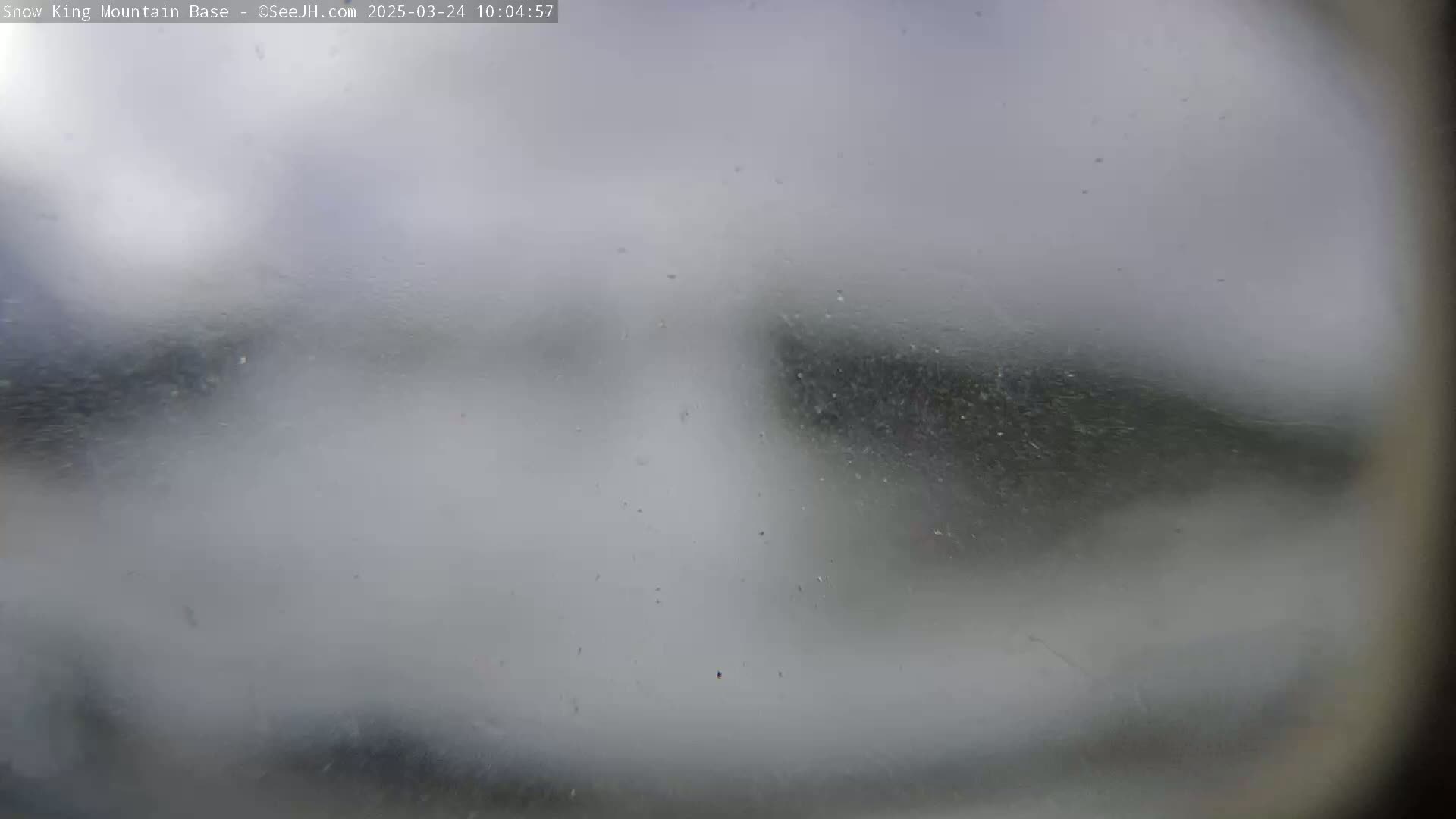 A blurry view of an indistinct landscape is seen through a rain-covered window.