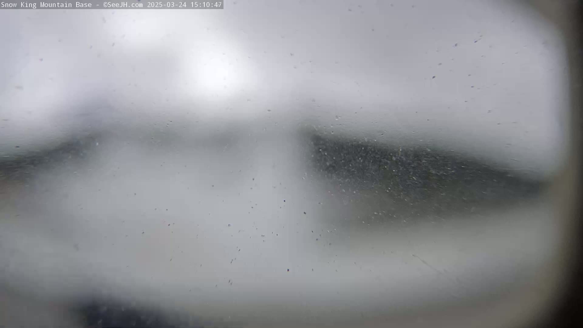 A blurry view of a snow-covered landscape is seen through a rain-covered window.