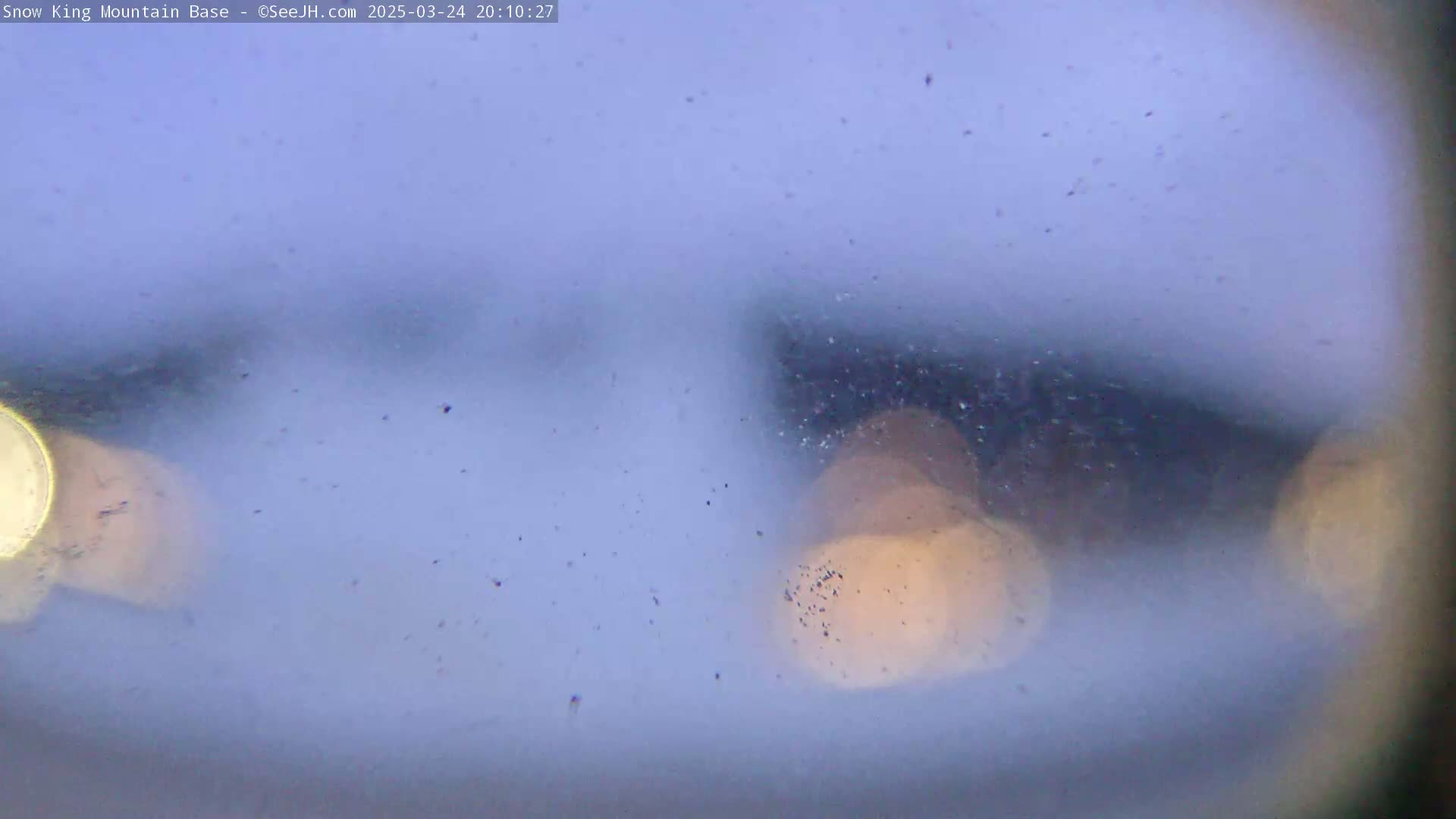 A blurry, snow-filled view of lights through a wet or frosted window.