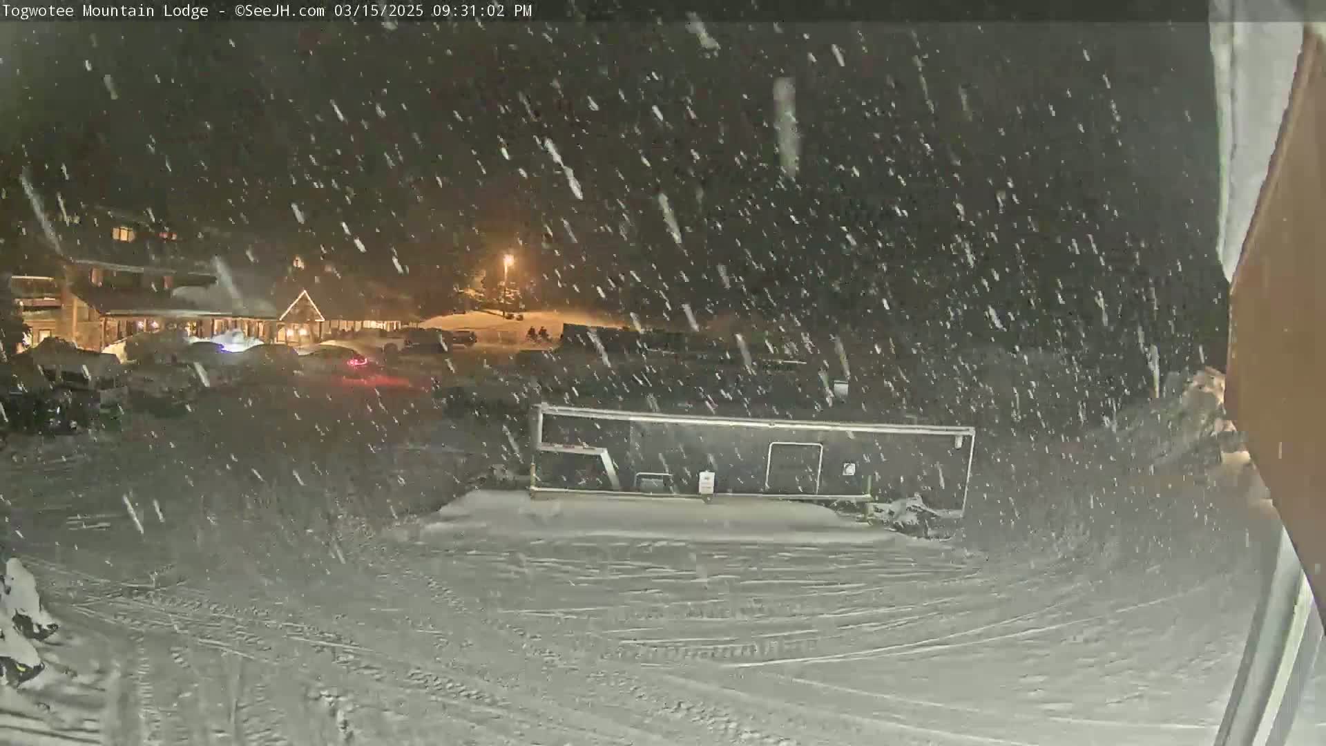 A snow-covered parking lot with cars and a building in the background during a heavy snowfall at night.