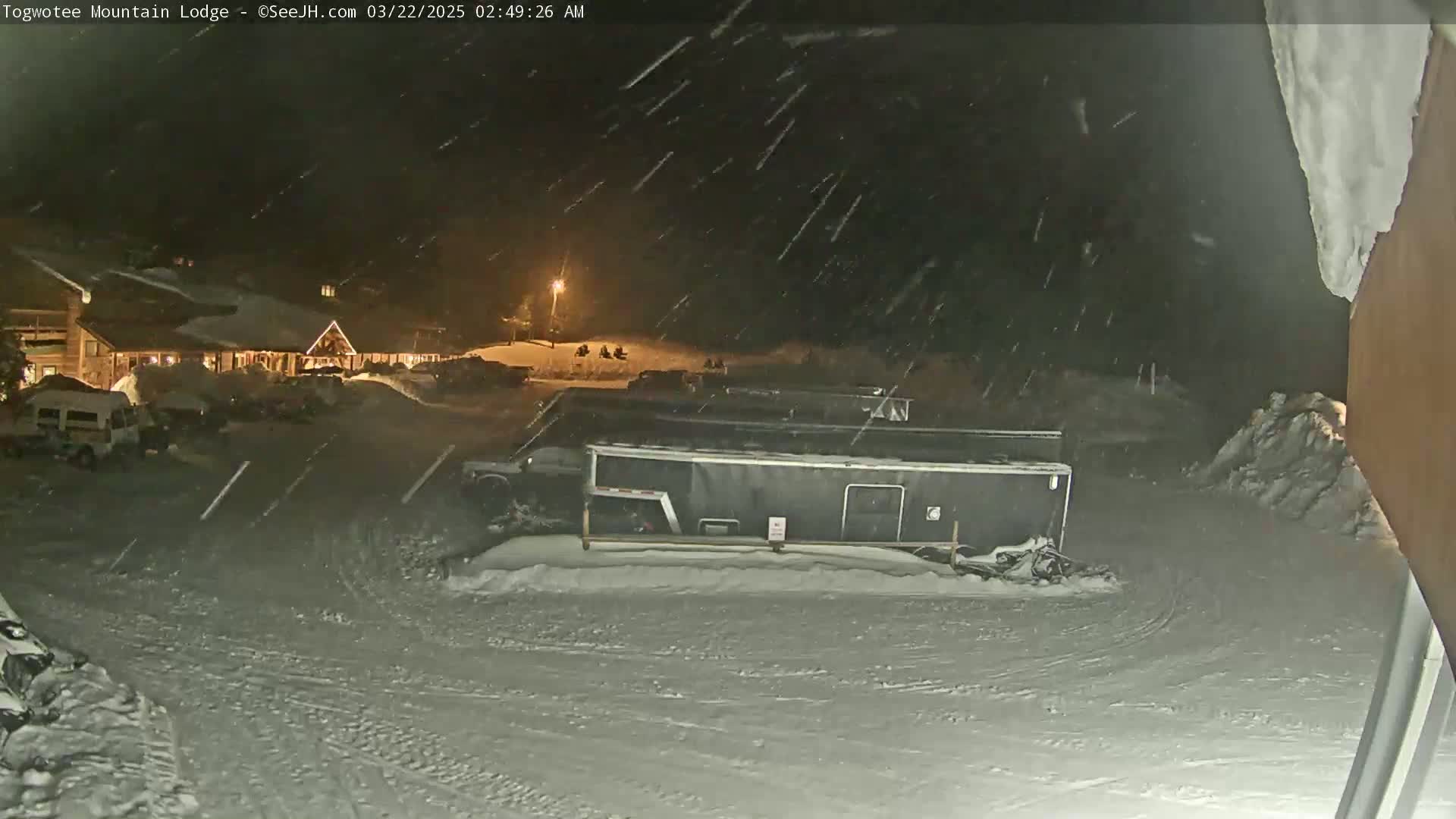 A snow-covered parking lot at night with a lodge in the background, under heavy snowfall.