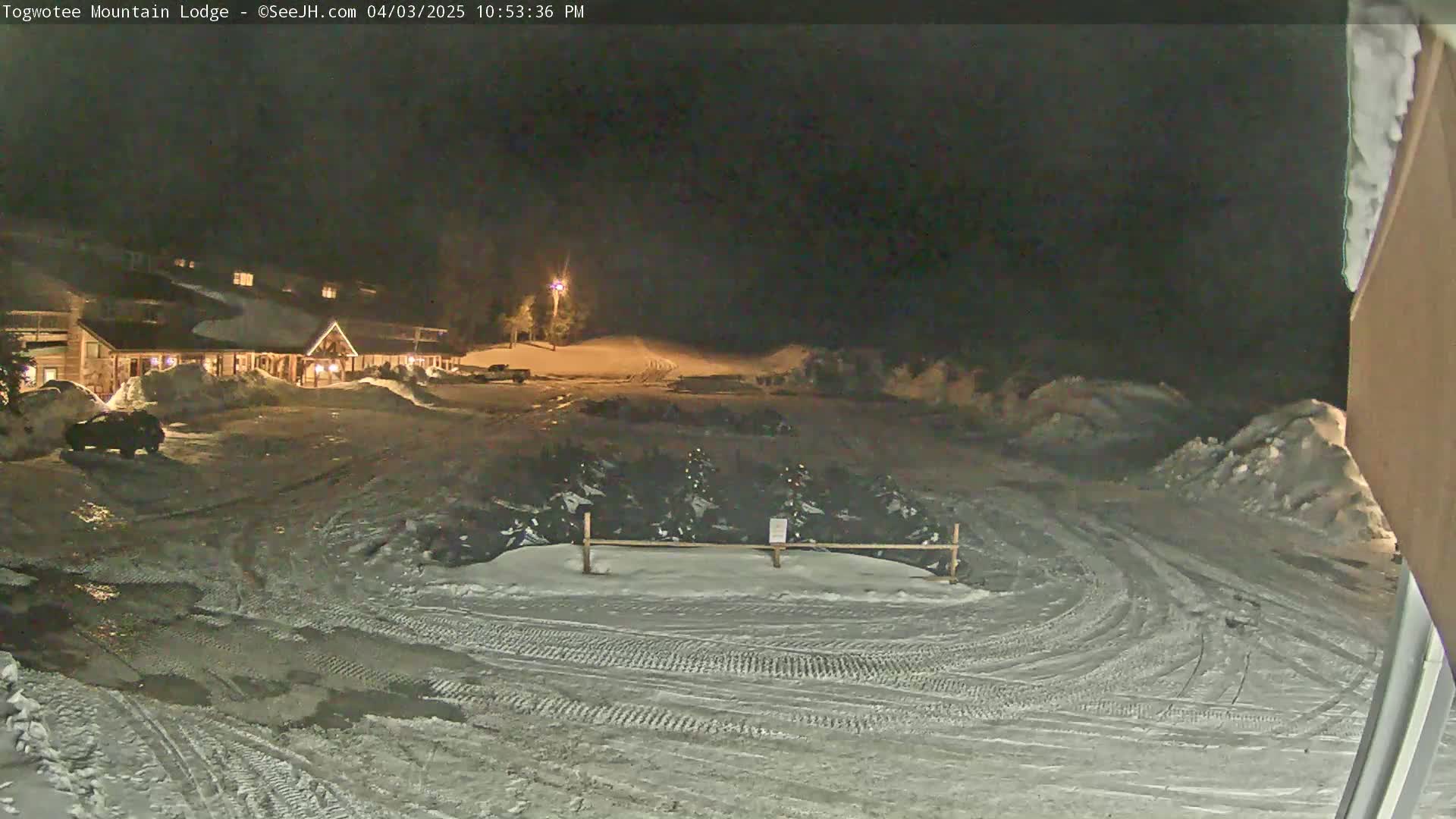 A snow-covered parking lot at night, with a lodge illuminated in the background under a dark sky.