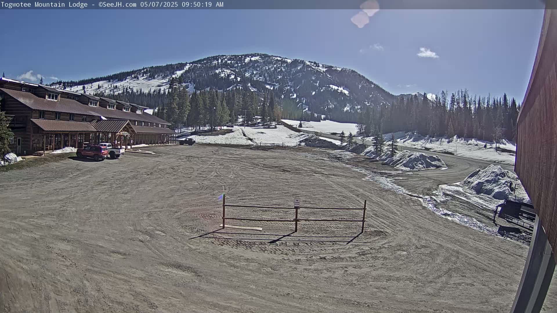 A lodge sits in a parking lot next to a snow-dusted mountain under a mostly sunny sky.