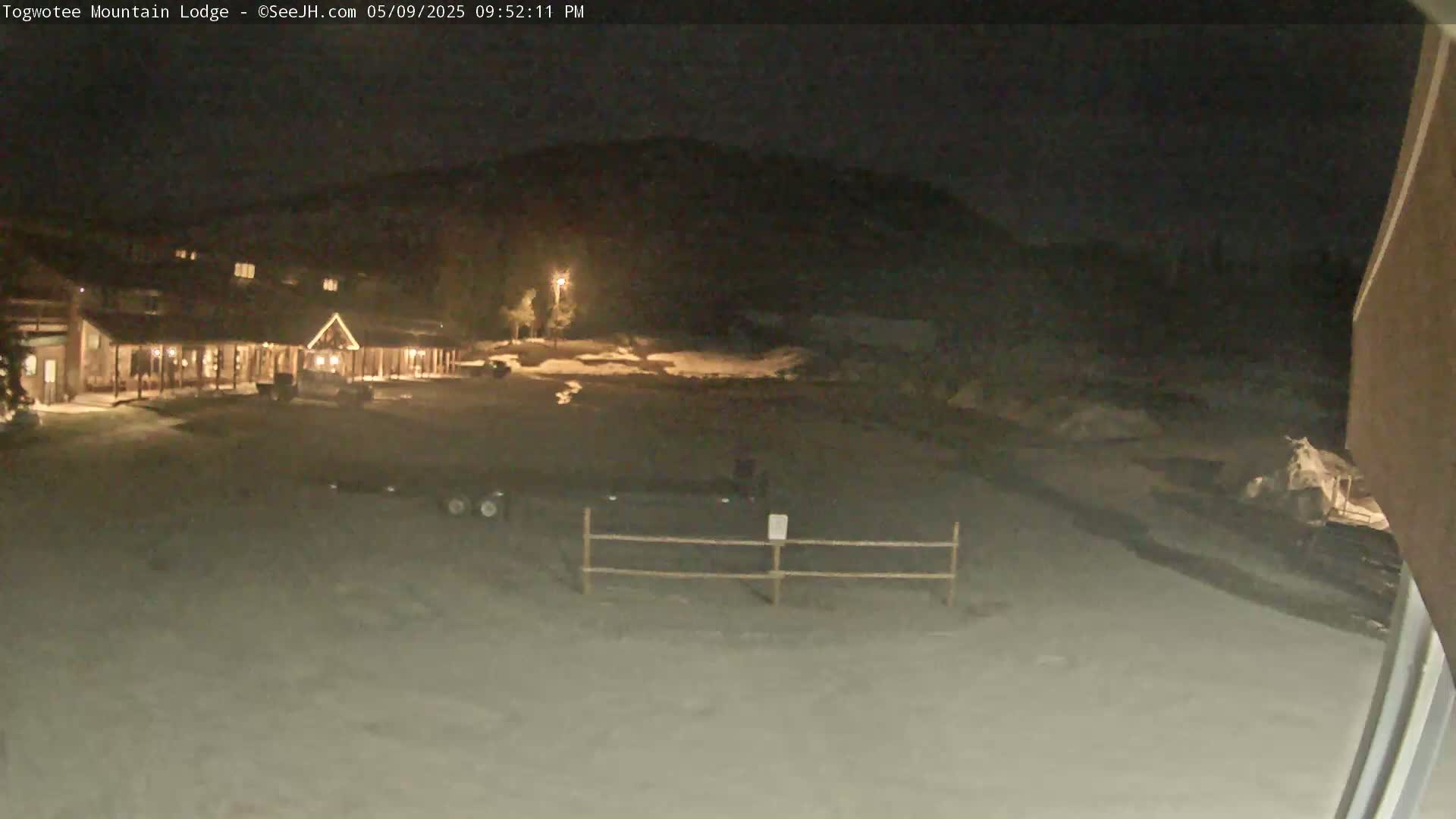 A snow-covered lodge is illuminated at night, with a few vehicles visible in the parking lot.