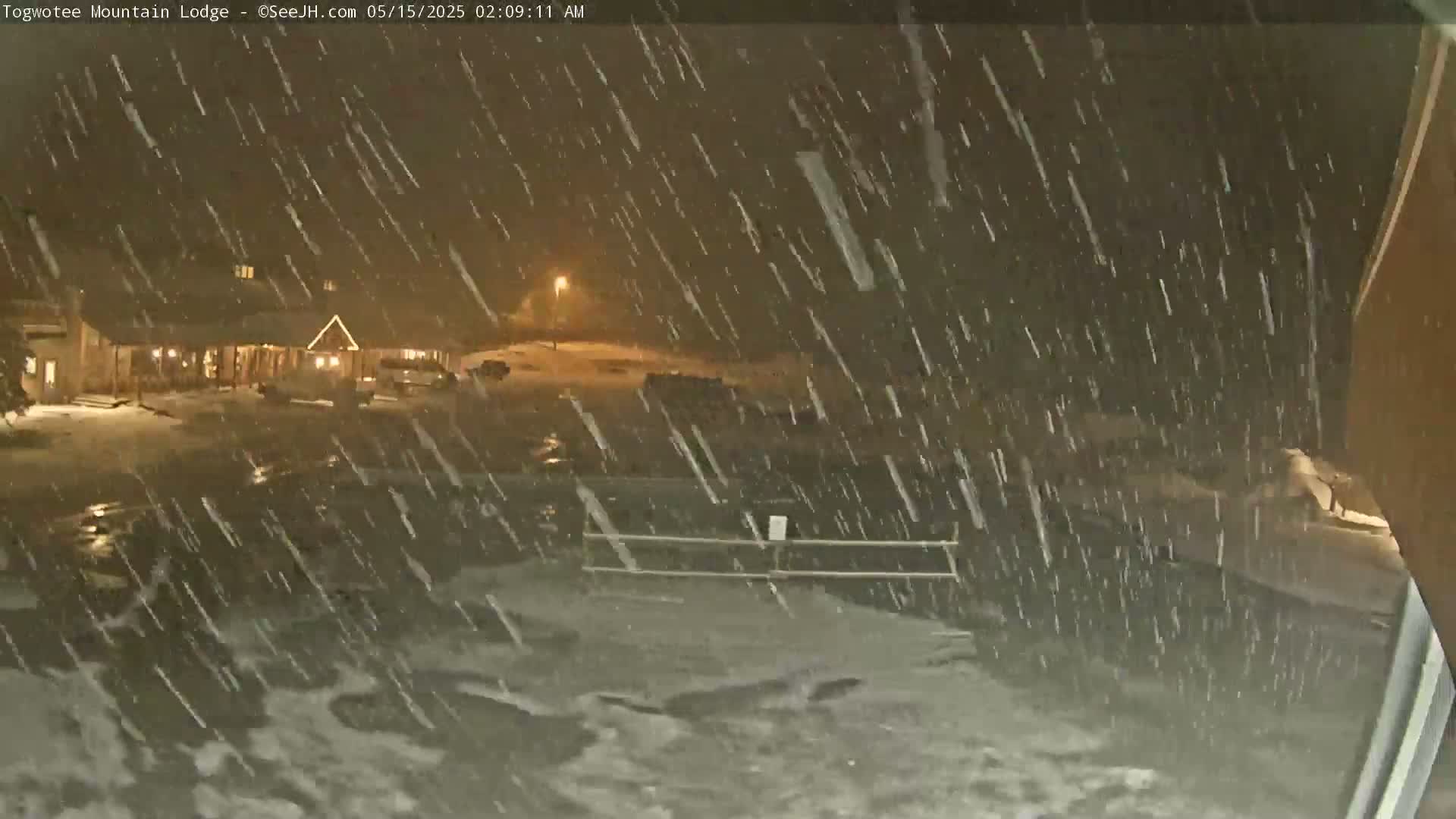 A snowstorm at night blankets a lodge and its parking lot in a layer of snow.