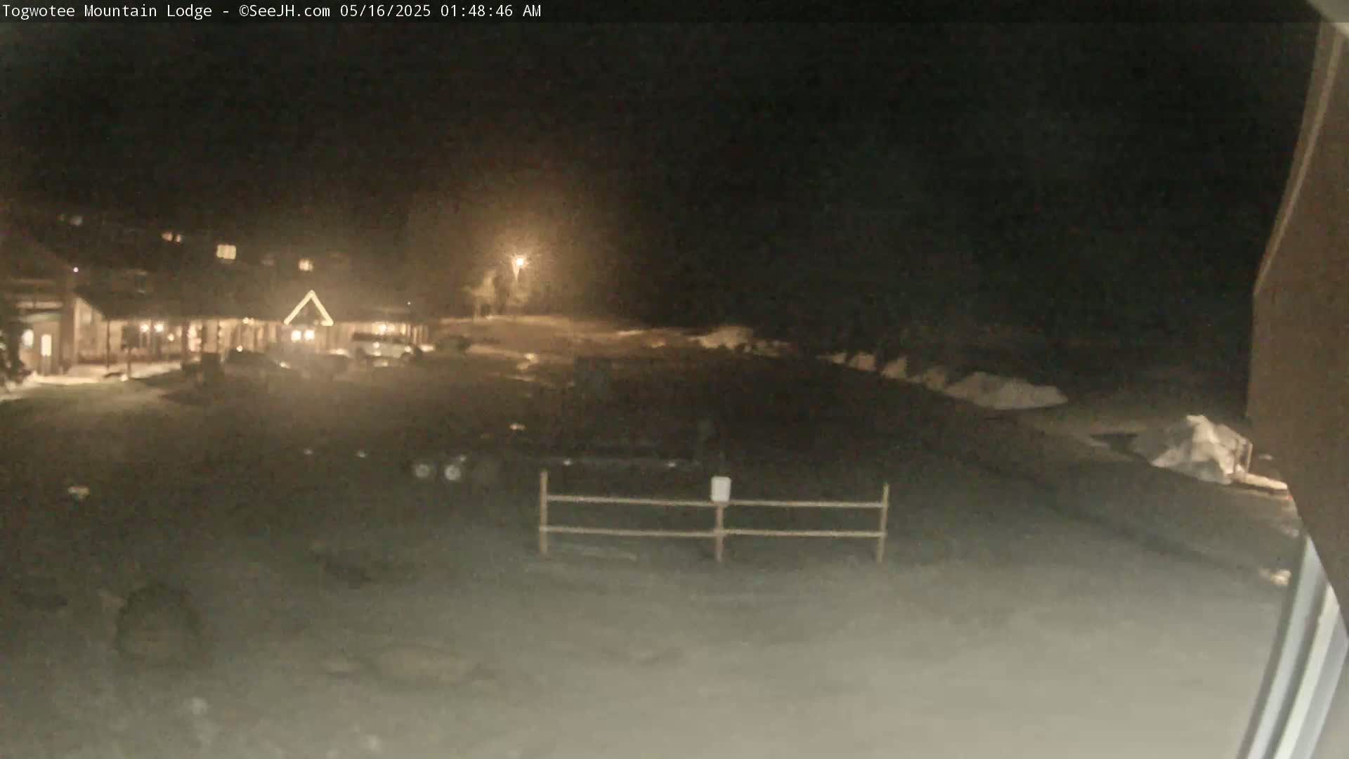 A dimly lit, snow-covered parking lot in front of a lodge at night.