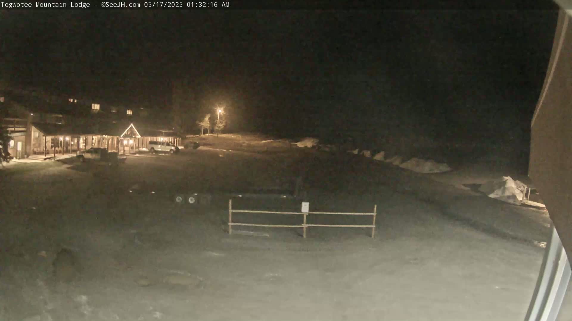 A nighttime view of a lodge and its parking lot, covered in snow, under a dark sky.