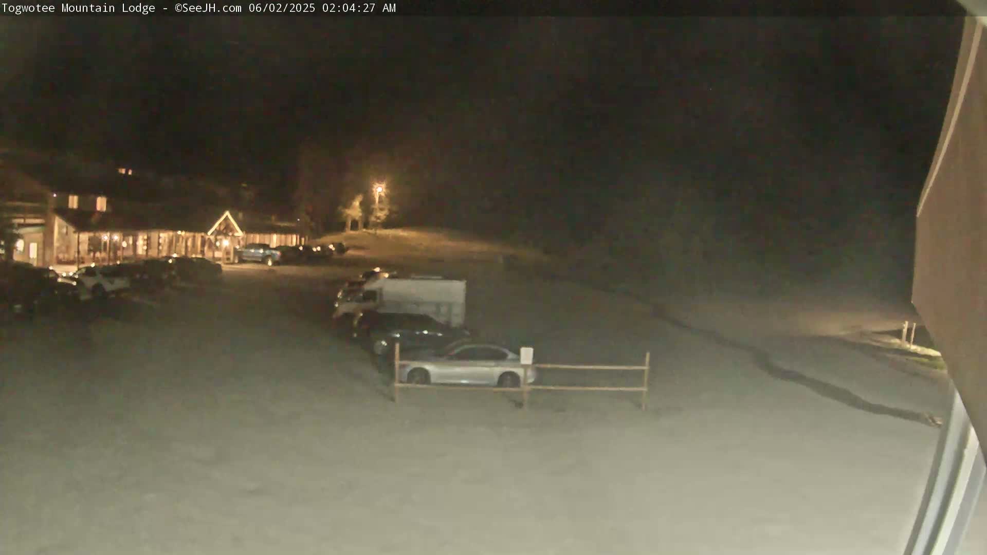 A nighttime view of a lodge with a parking lot containing several vehicles, under dark, clear skies.