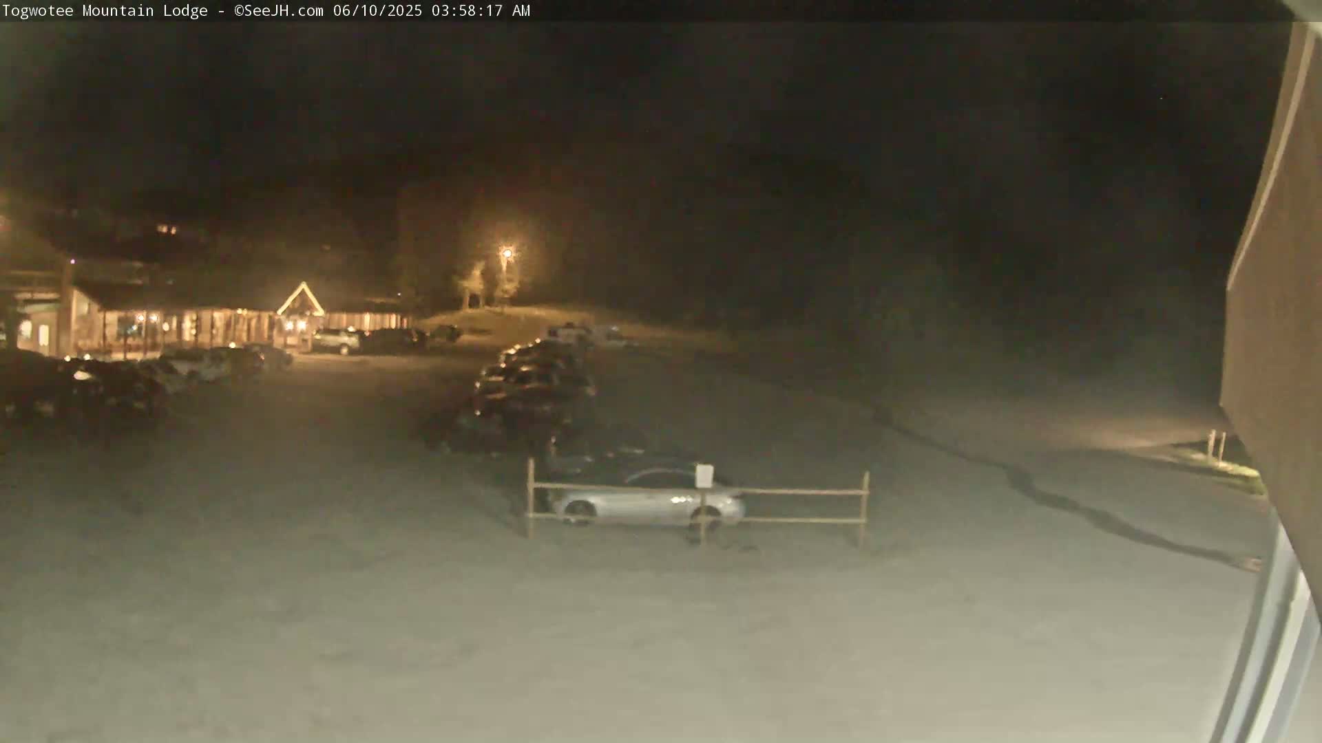 A nighttime view of a lodge parking lot with cars parked and a snow-covered ground.