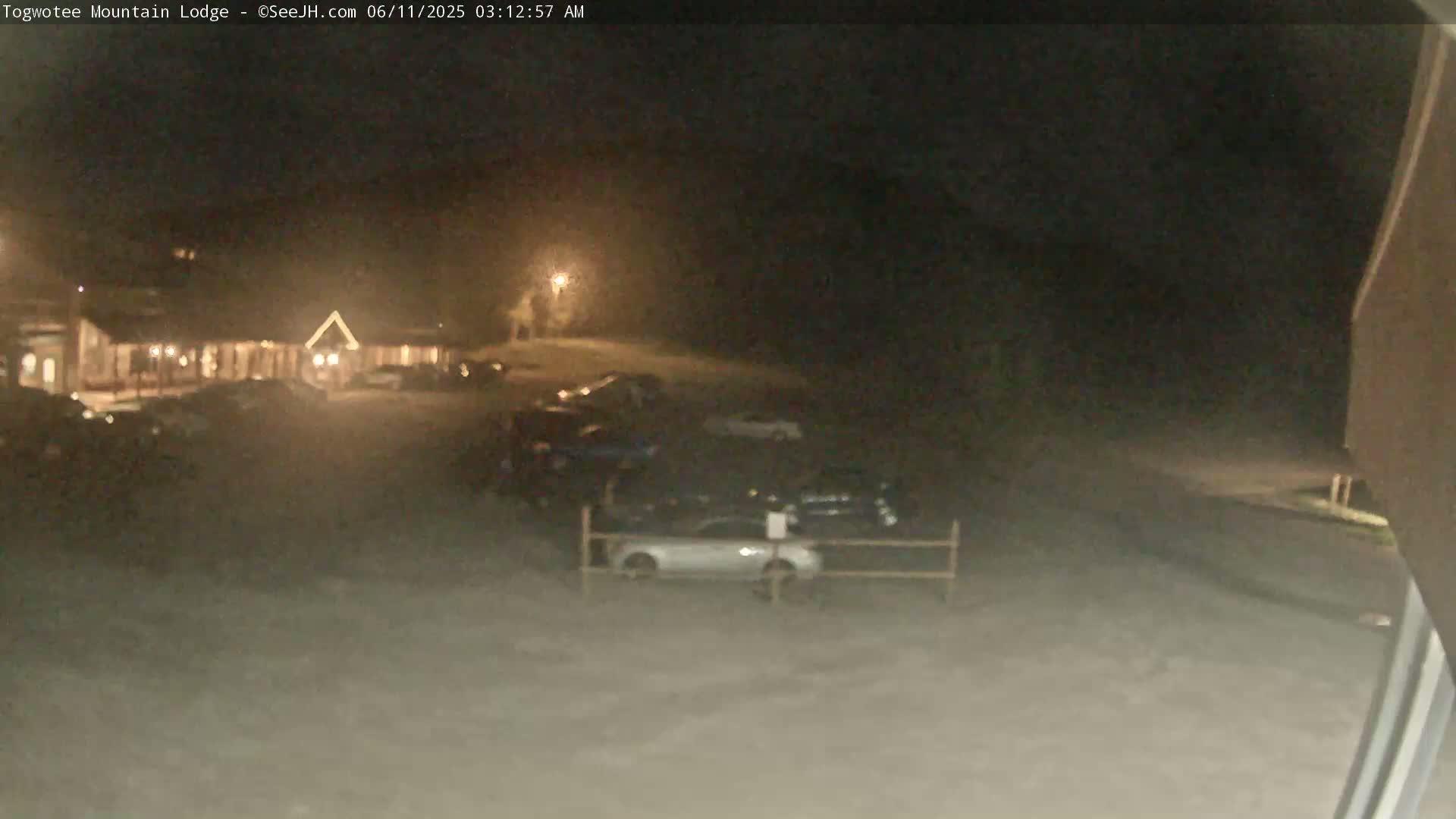 A nighttime view of a snow-covered parking lot in front of a building, with several cars parked.